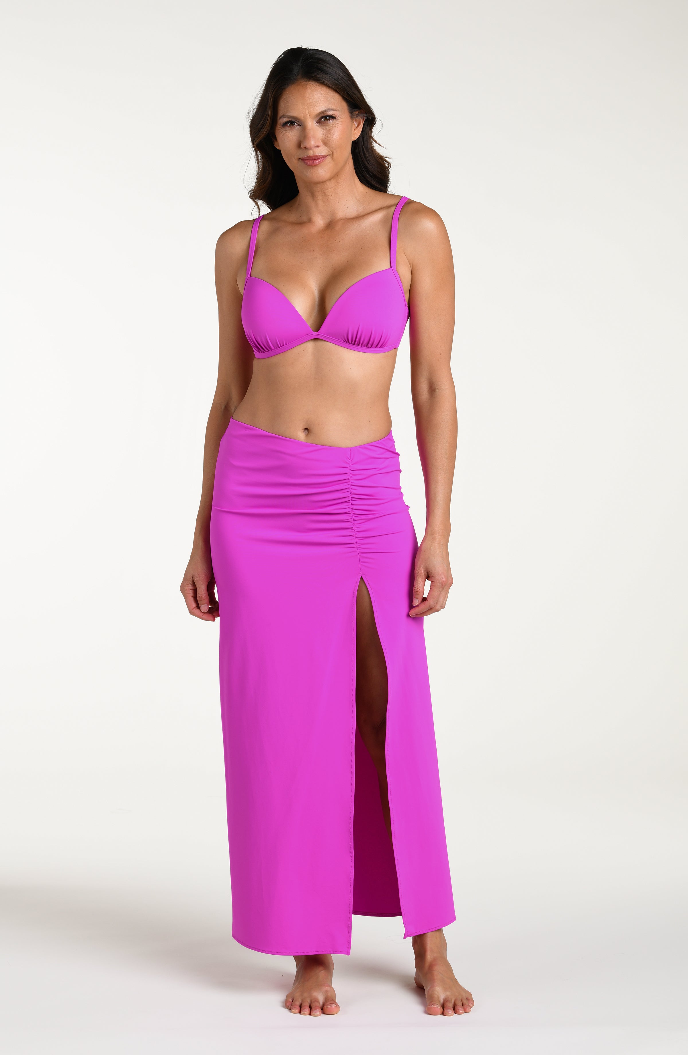 Woman wearing a violet colored bikini top and matching maxi skirt against a white background. 