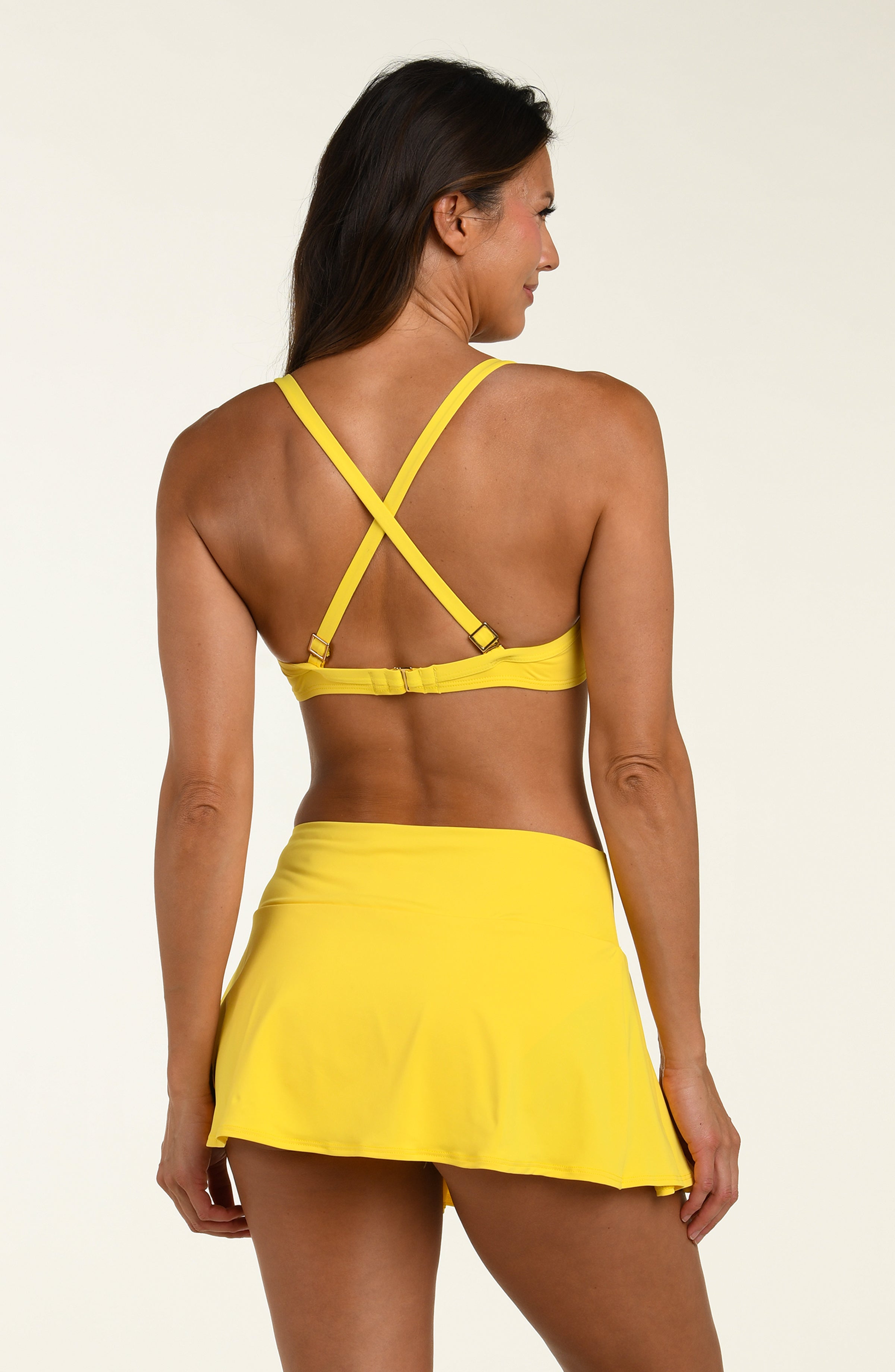 Woman wearing a yellow bikini top and matching swim skirt against a white background.