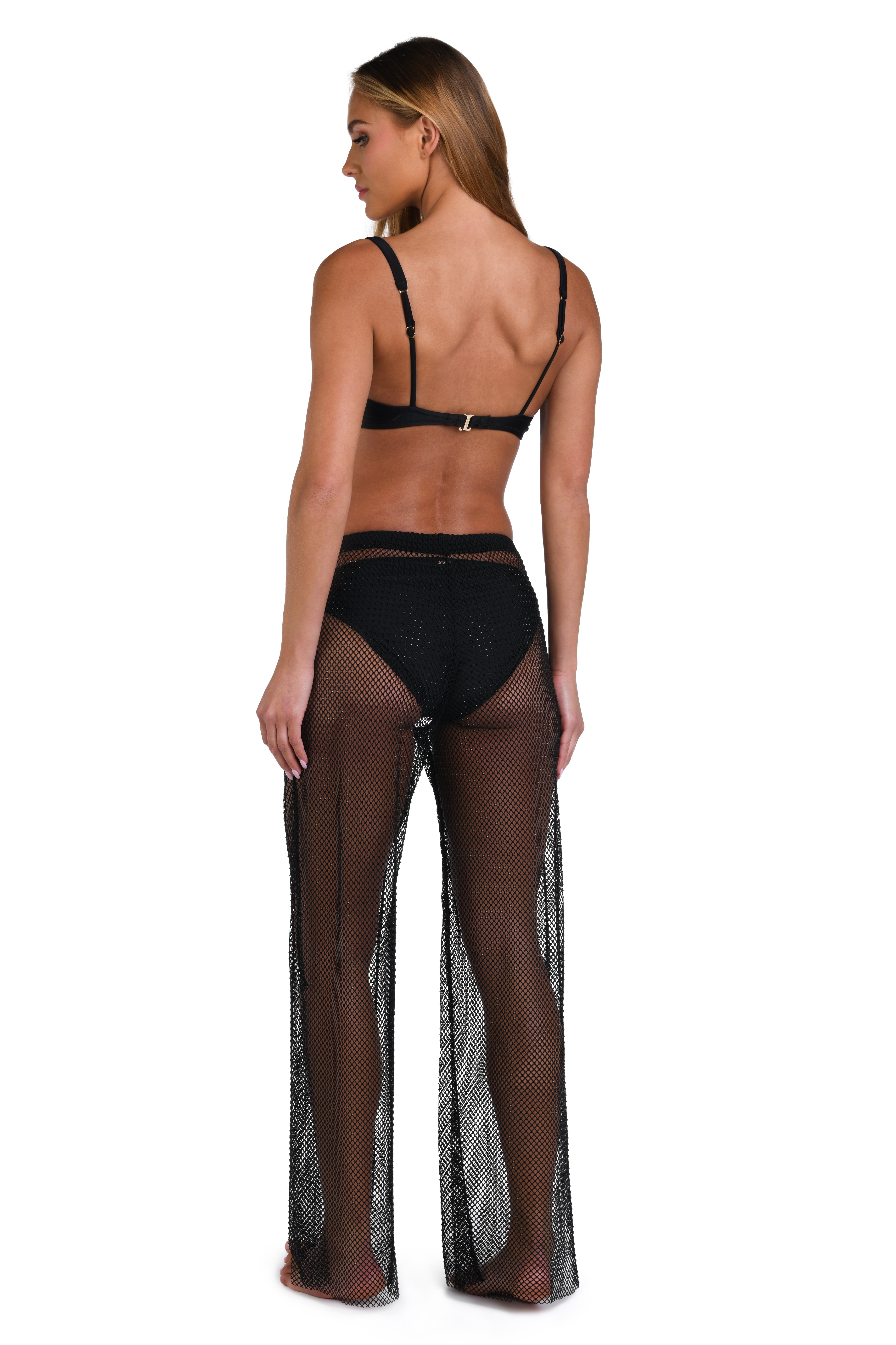 A woman shown from the back wearing sheer black fishnet wide-leg pants over black underwear, against a plain white studio background.
