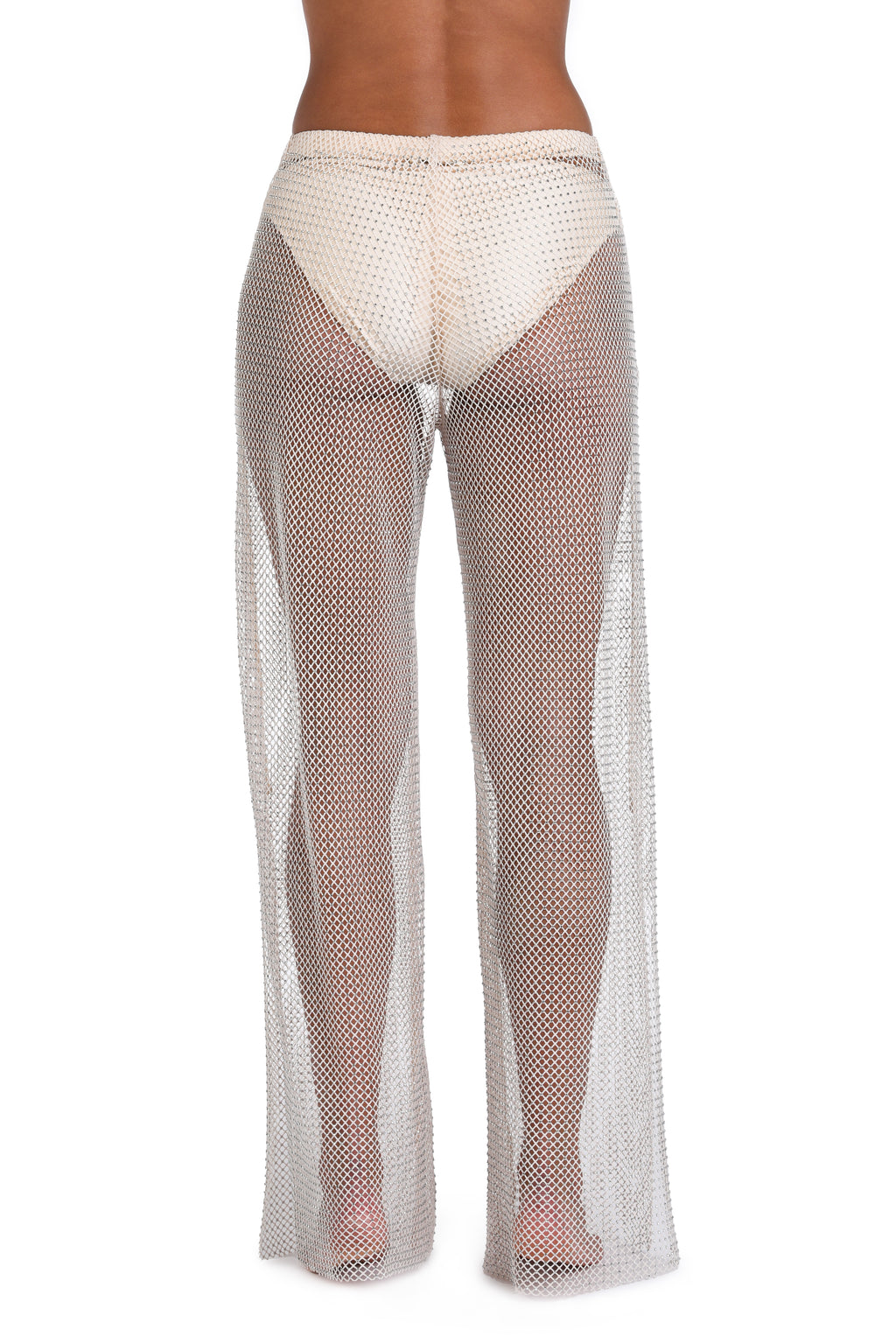 A model shown from the back wearing a sheer, wide-leg fishnet cover-up in a light beige or off-white color over cream underwear, set against a plain white background.