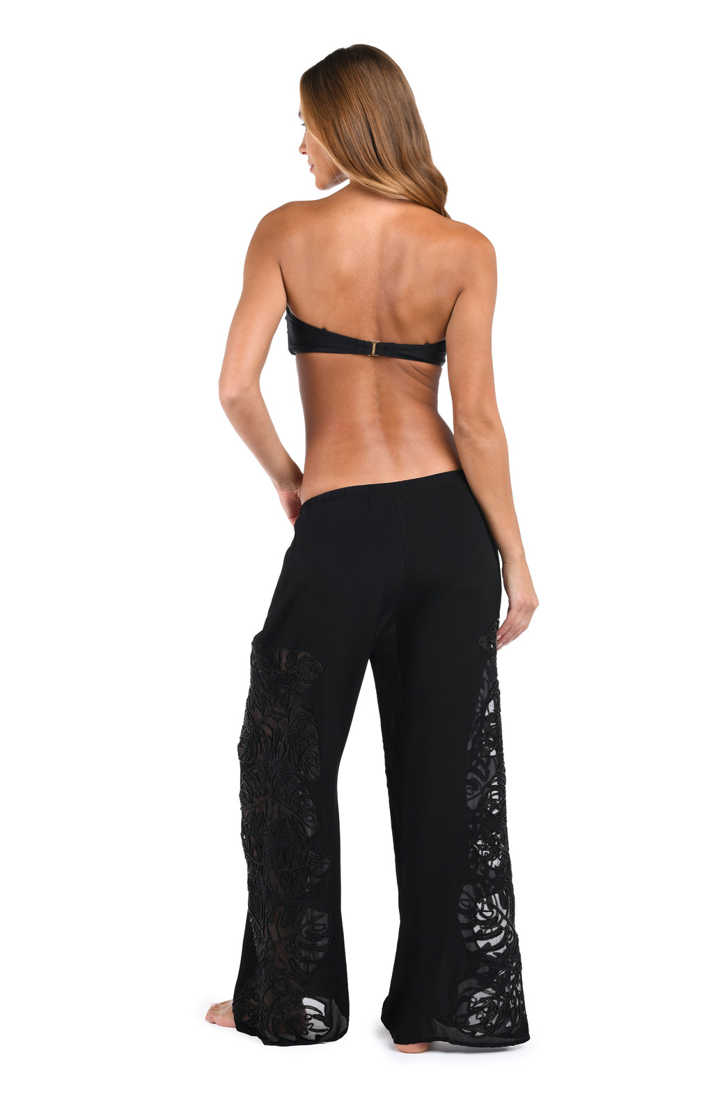 A woman shown from the back wearing black wide-leg pants with lace panels on the lower legs, paired with a black strapless bikini top, against a plain white background.