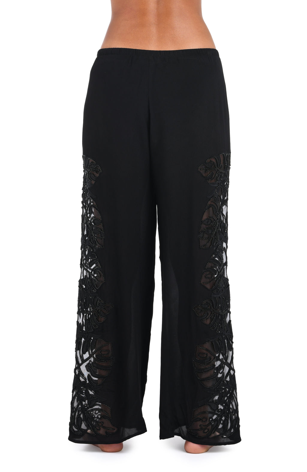 Black wide-leg pants with sheer floral lace panels down the sides, shown on a model from the waist down against a white background.