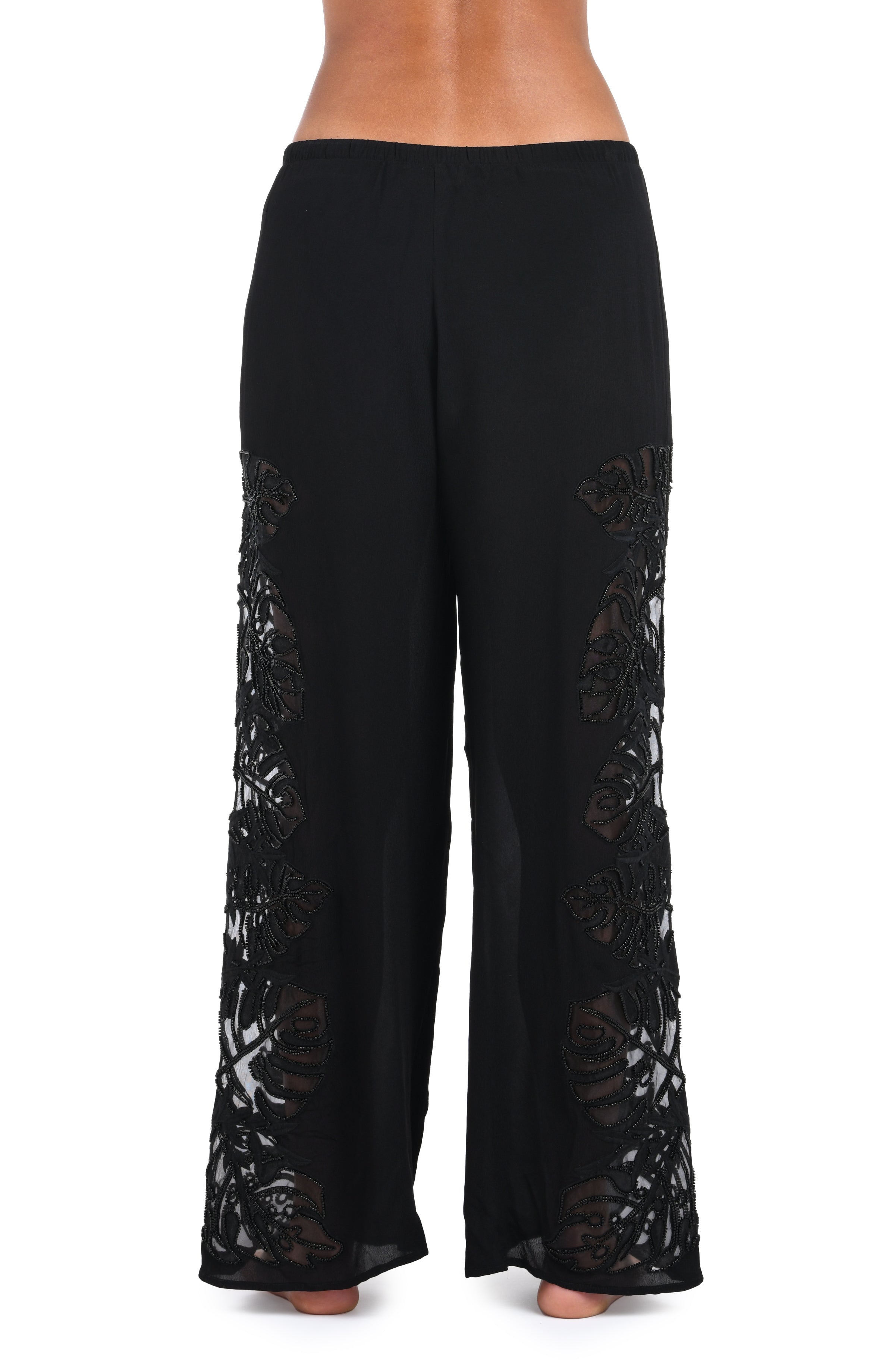 Black wide-leg pants with sheer floral lace panels down the sides, shown on a model from the waist down against a white background.