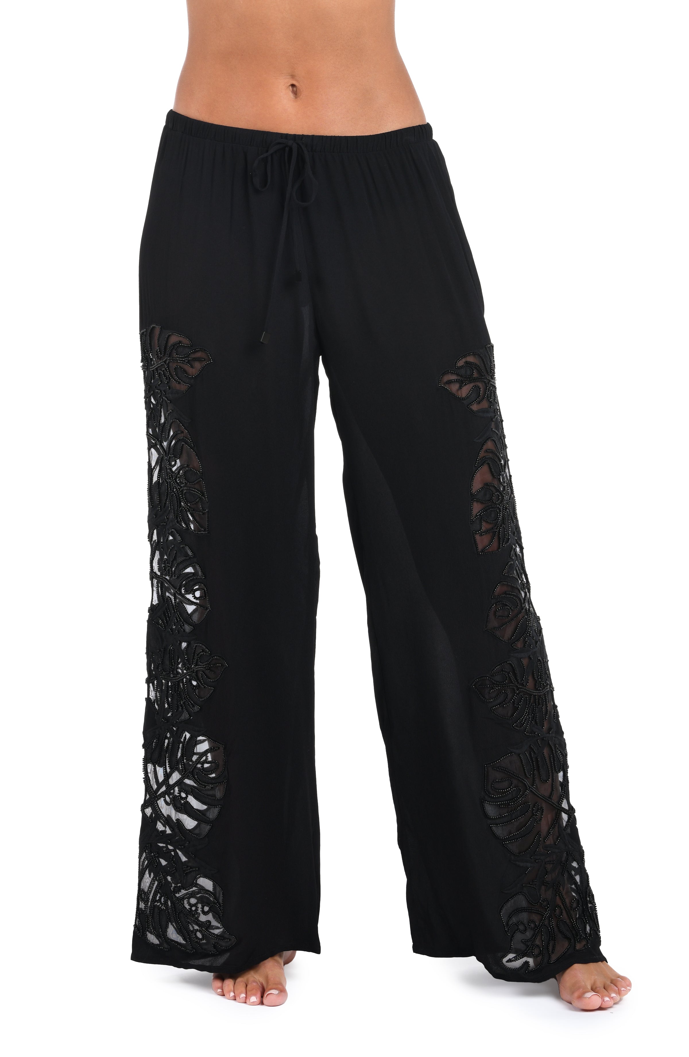 Black wide-leg pants with floral lace cutout details on the sides, shown on a model against a white background.