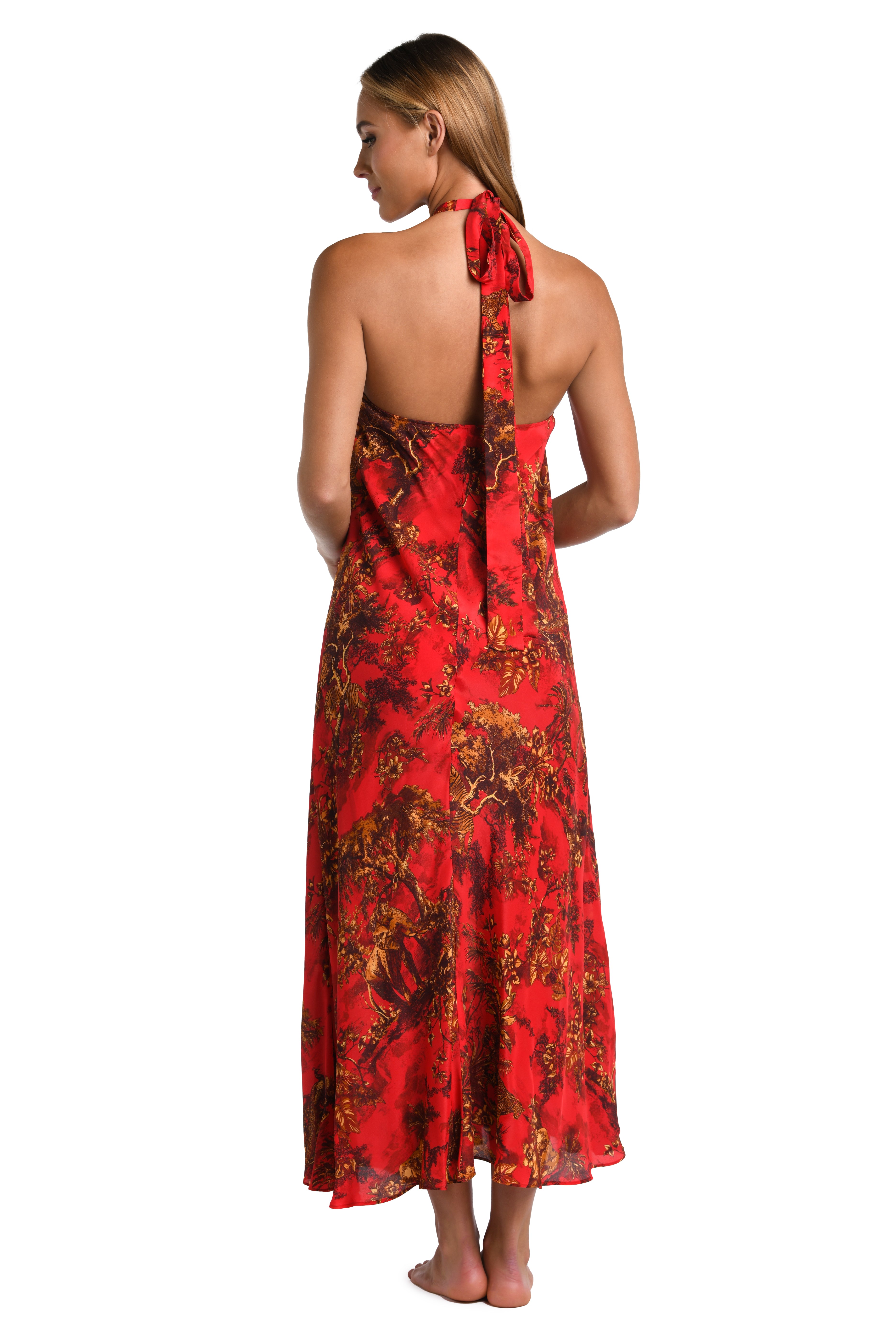 A woman shown from the back wearing a red halter maxi dress with a dark floral print, standing against a plain white background.