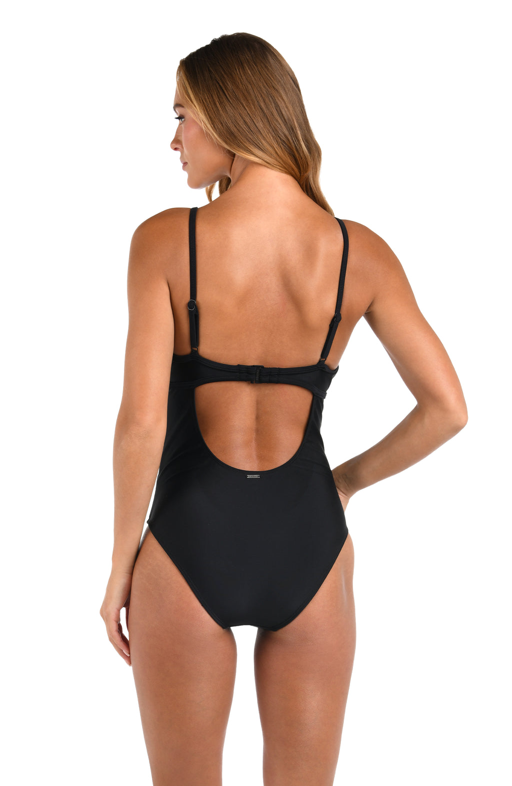 A woman shown from the back wearing a black one-piece swimsuit with thin shoulder straps and a large open back cutout, photographed against a plain white studio background.