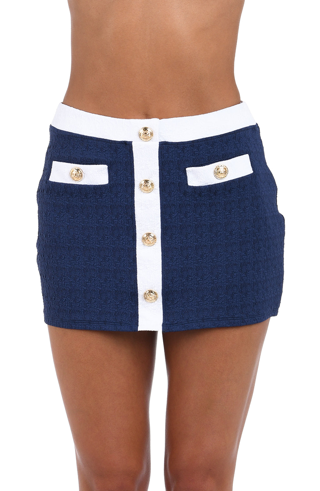 A close-up of a model wearing a navy blue textured tweed mini skirt with a white center panel, white waistband, and white pocket flaps accented with gold-tone buttons.