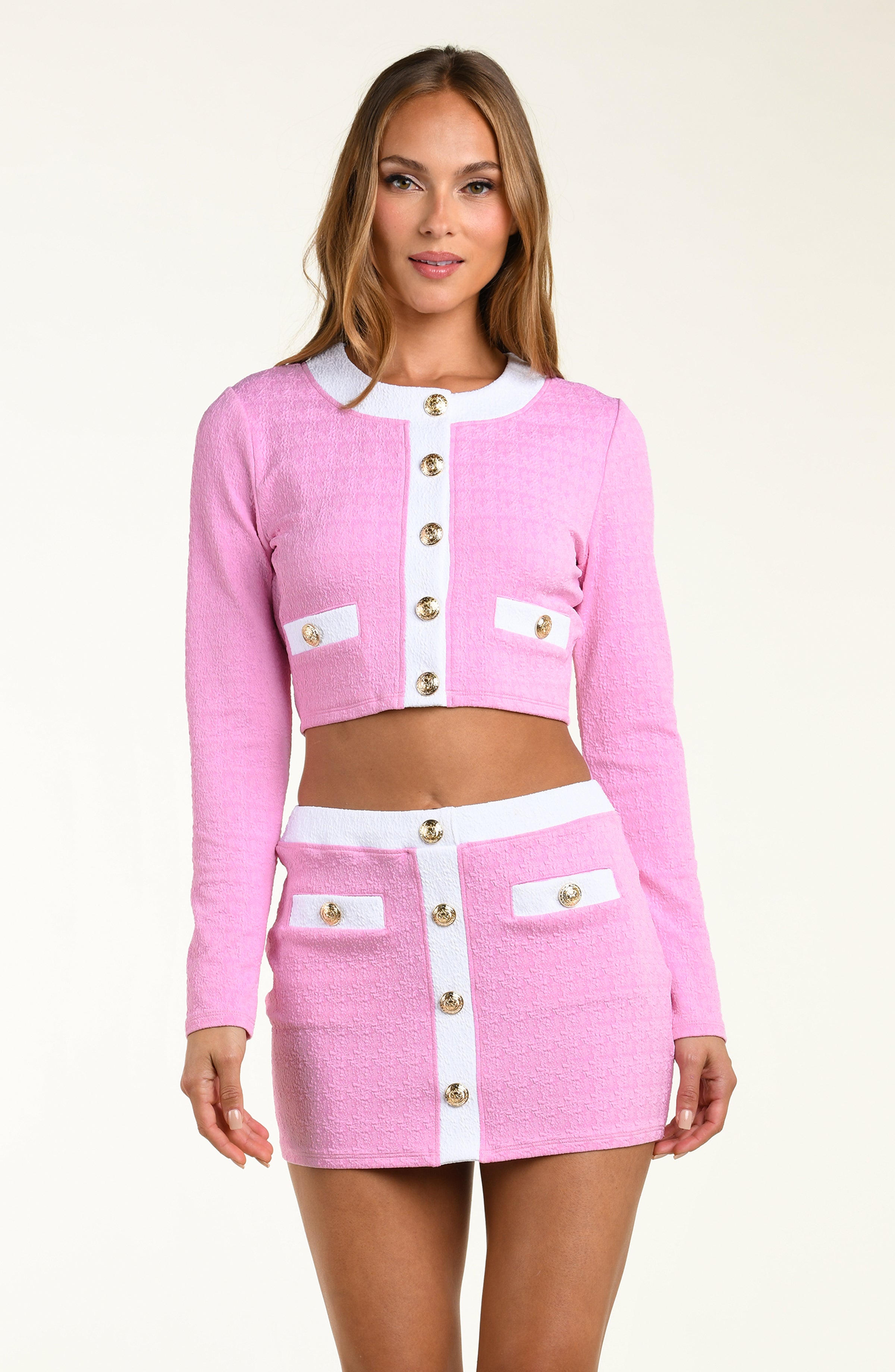 Woman wearing a pink and white outfit with gold buttons on a beige background