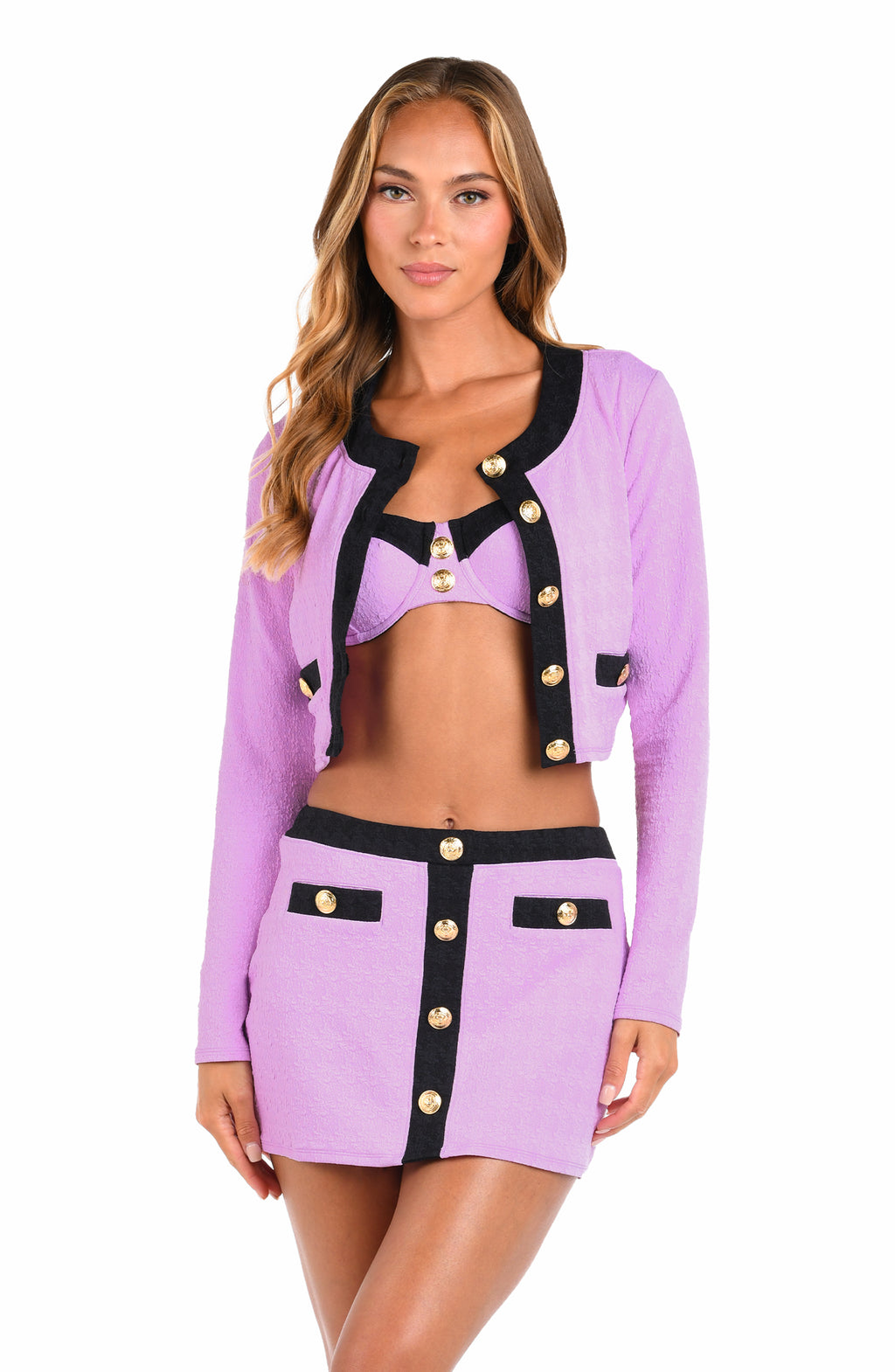 A model wearing a lavender and black two-piece set consisting of a long-sleeve cropped jacket with gold buttons and a matching mini skirt with a black center panel and gold buttons.
