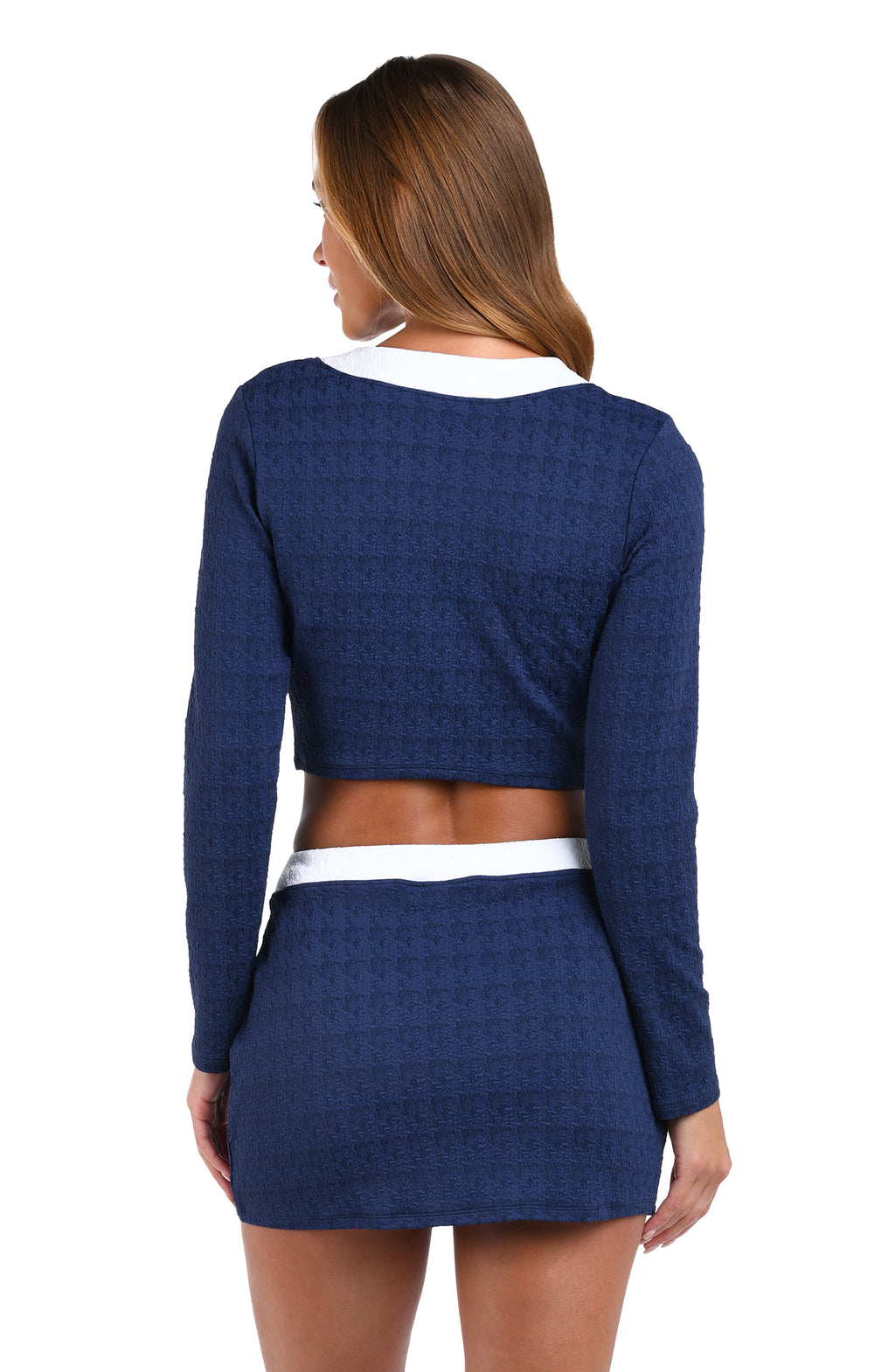 A woman shown from the back wearing a navy blue textured long-sleeve crop top and matching mini skirt with white contrast trim, against a plain white background.