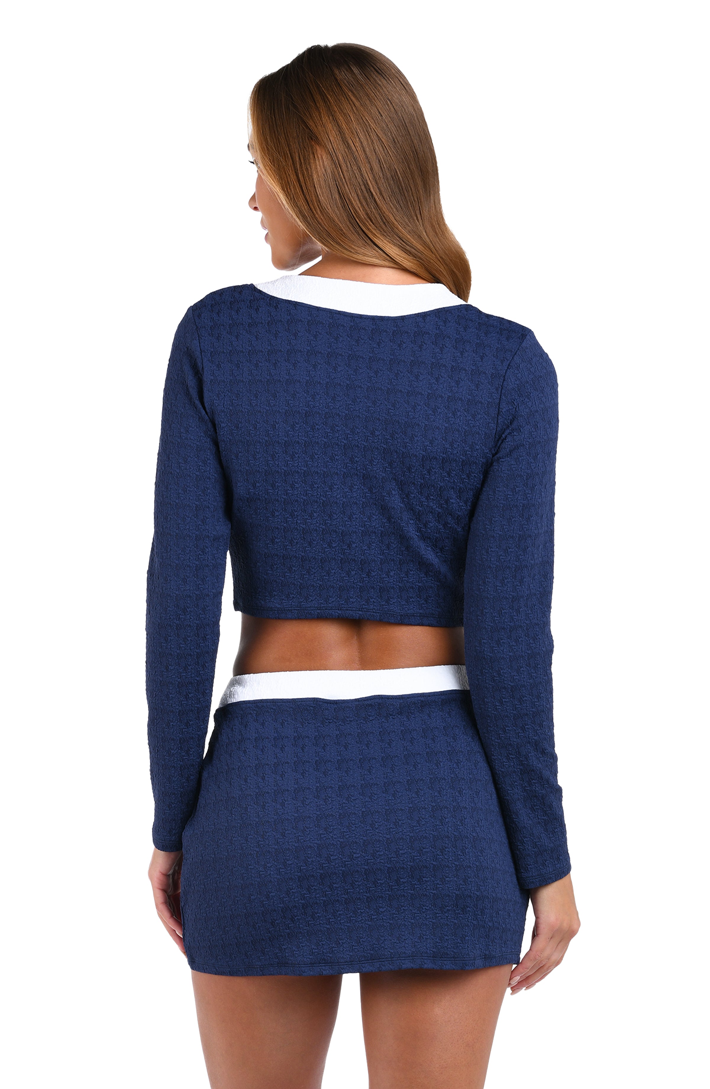 A woman shown from the back wearing a navy blue textured long-sleeve crop top and matching mini skirt with white contrast trim, against a plain white background.