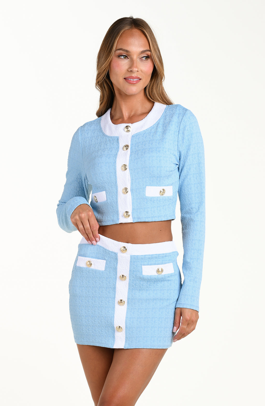 Woman wearing a light blue cardigan and skirt set with white buttons on a white background