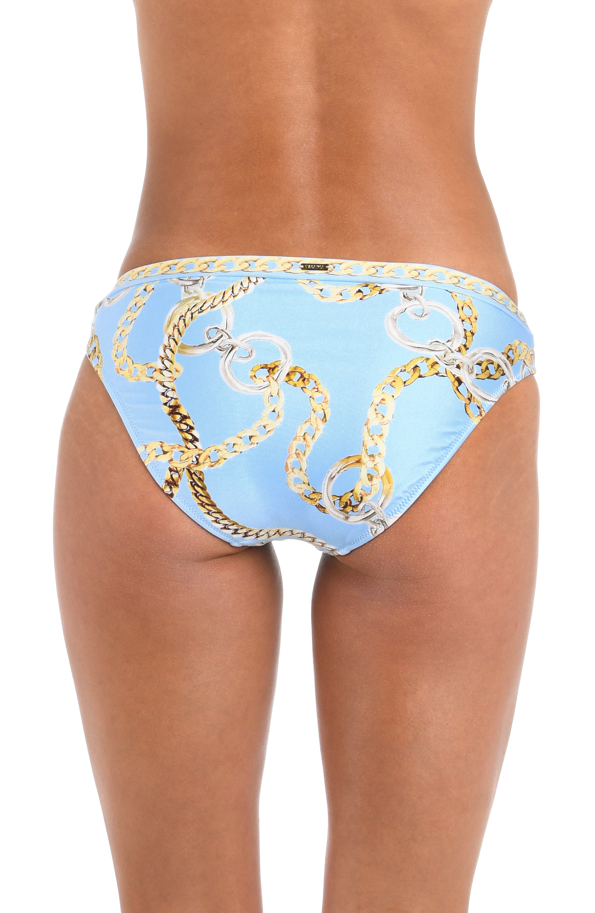 A woman wearing light blue bikini bottoms with a gold chain print and a bow detail on the front, set against a plain white background.