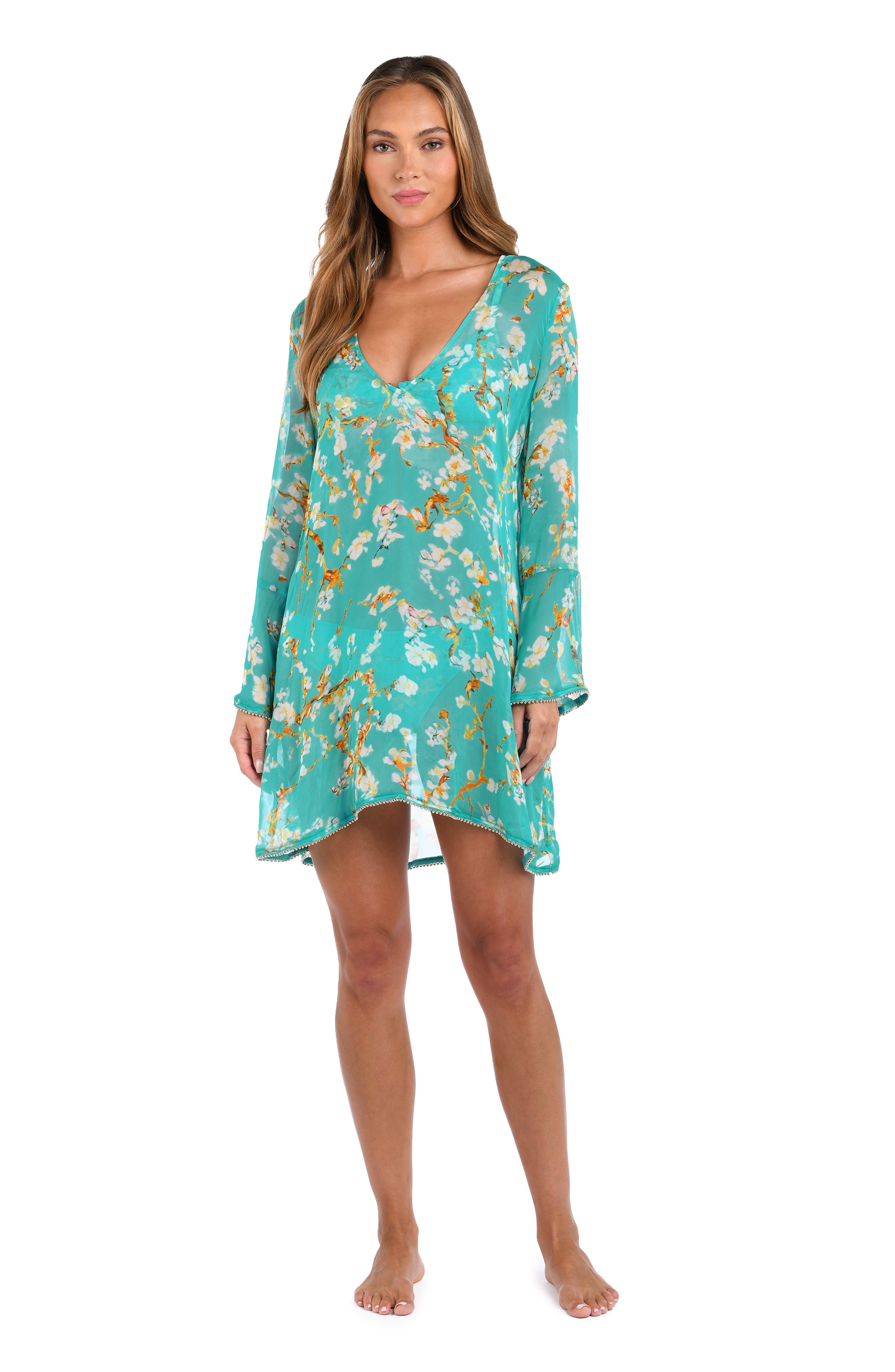 A woman modeling a long-sleeve, V-neck sleep shirt or cover-up in a turquoise floral print with yellow and white flowers, set against a plain white background.