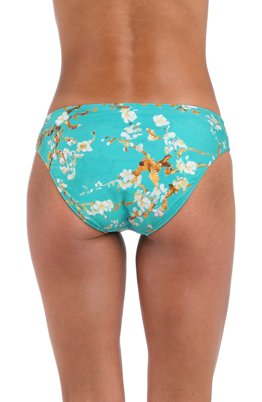 Rear view of a model wearing bikini bottoms with a turquoise blue background and an allover floral print in white and gold.