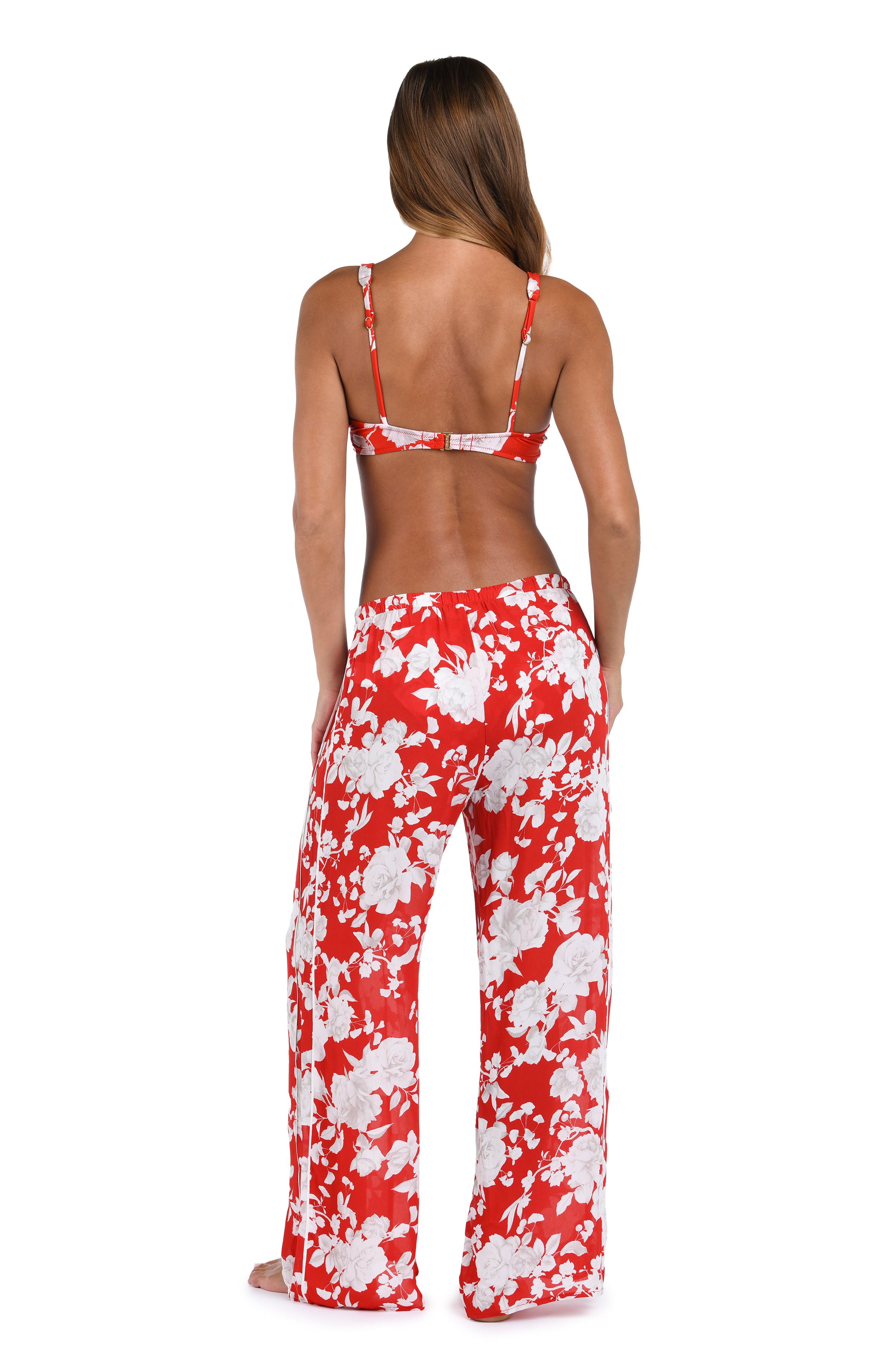 Woman wearing red multicolored floral printed cover up pants and a matching bikini top against a white background. 