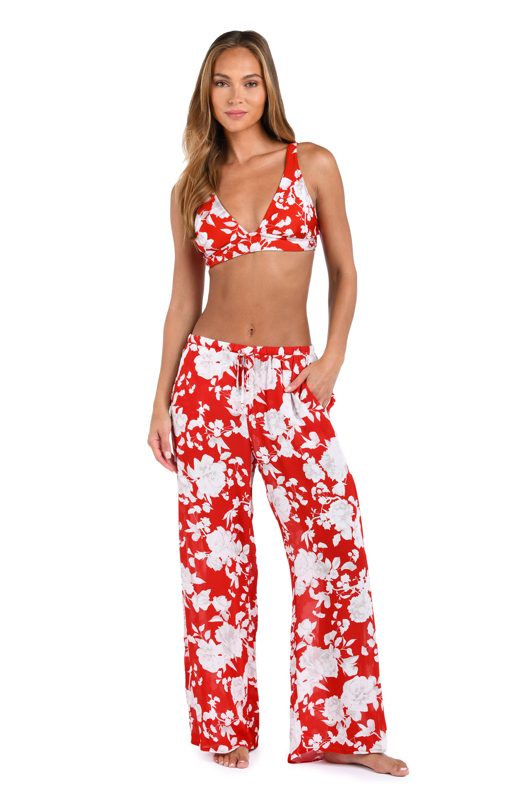 Woman wearing red multicolored floral printed cover up pants and a matching bikini top against a white background. 