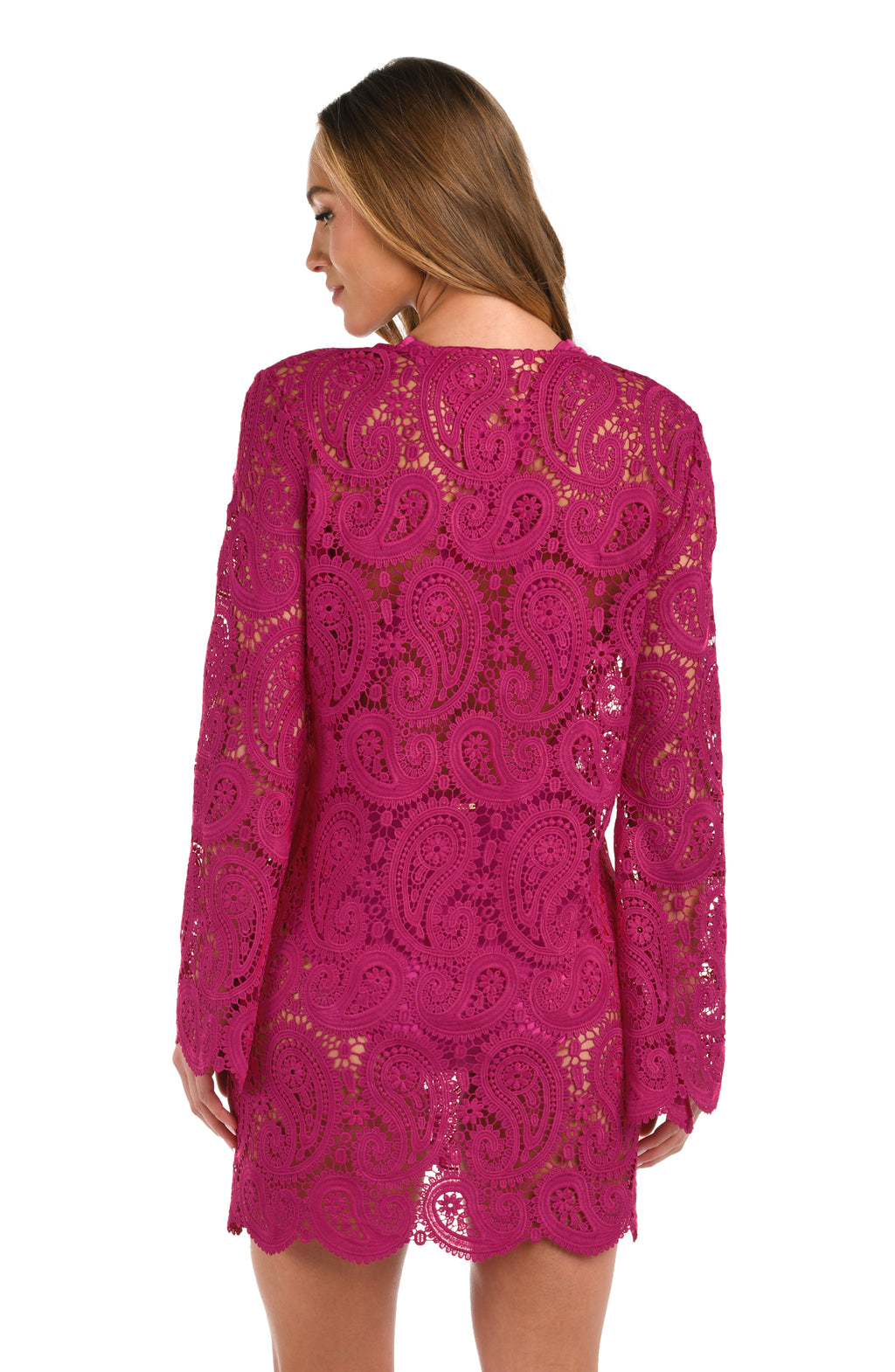 A woman wearing a fuchsia lace long-sleeve mini dress with a tie-neck detail, set against a plain white background.