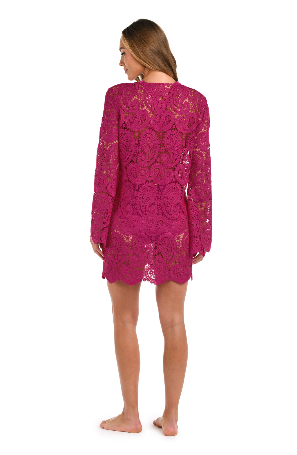 A woman wearing a fuchsia lace long-sleeve mini dress with a tie-neck detail, set against a plain white background.
