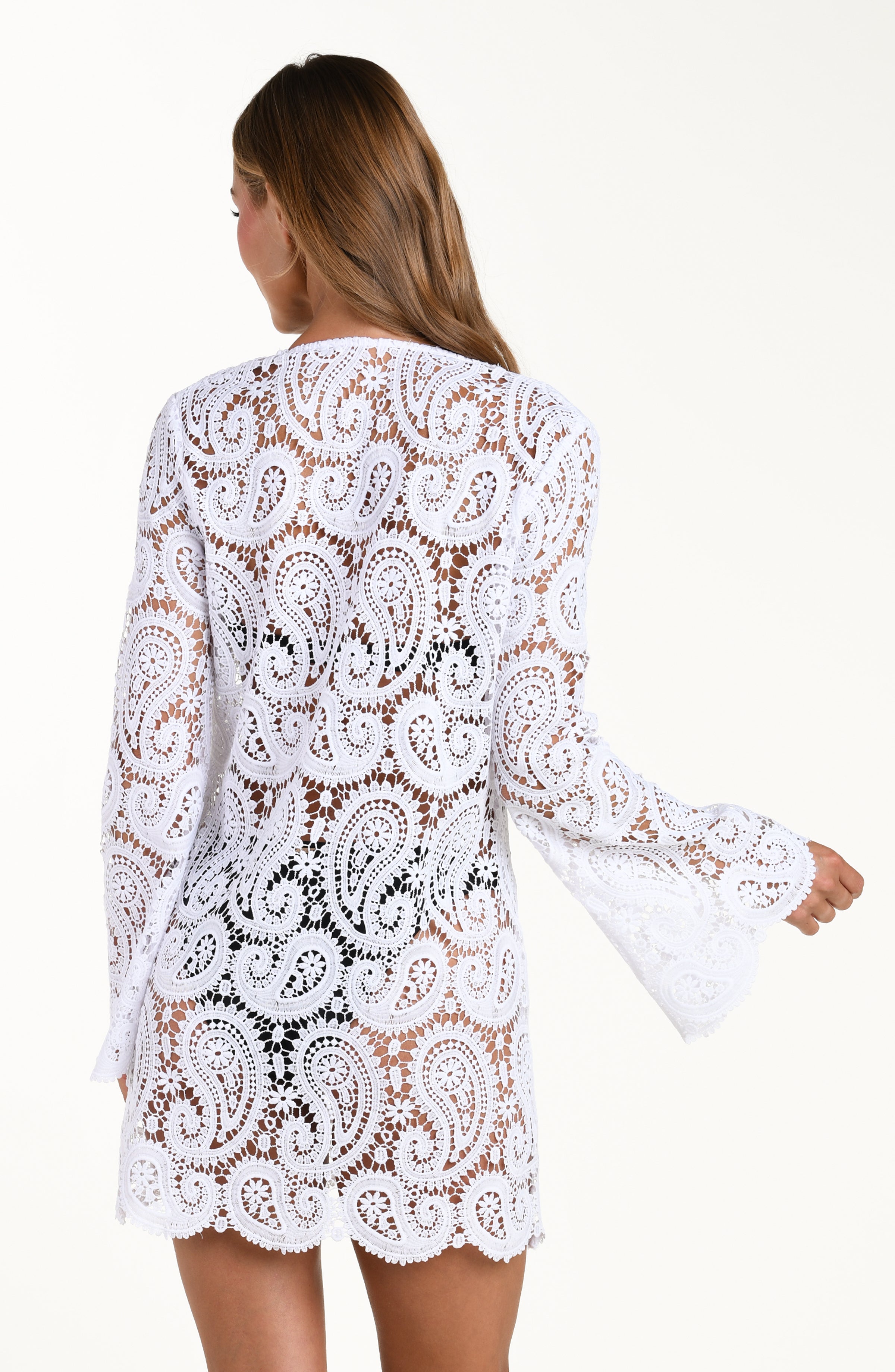 Woman wearing a white lace long sleeve dress against a white background. 