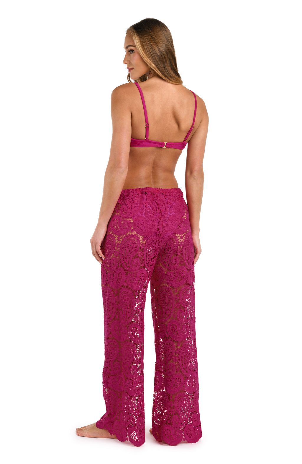 A person wearing bright fuchsia lace wide-leg pants with a drawstring waist  and matching bikini top against a white background.