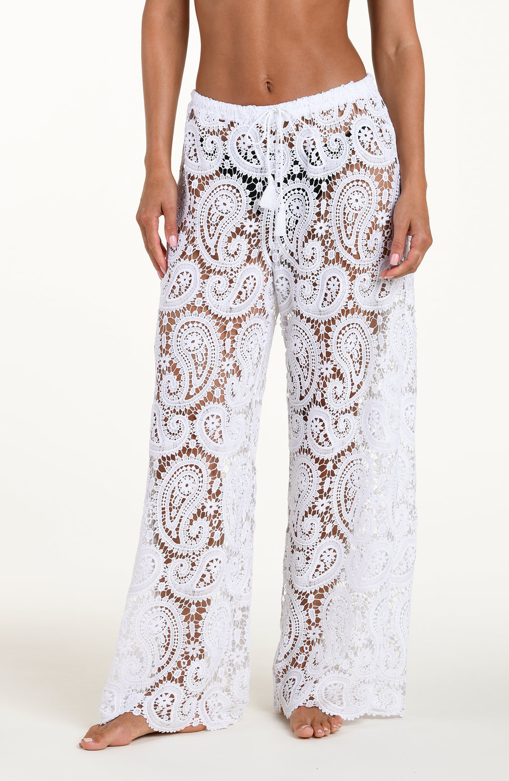 Woman wearing white crochet pants against a white background. 