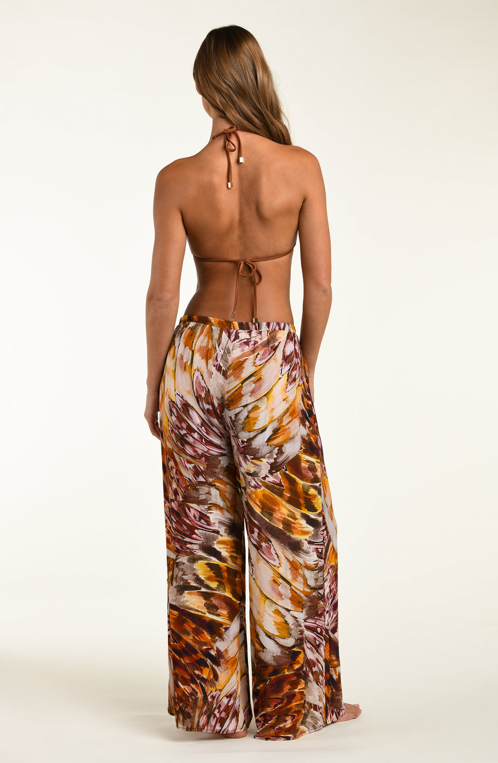 Woman wearing a backless top and patterned pants on a white background