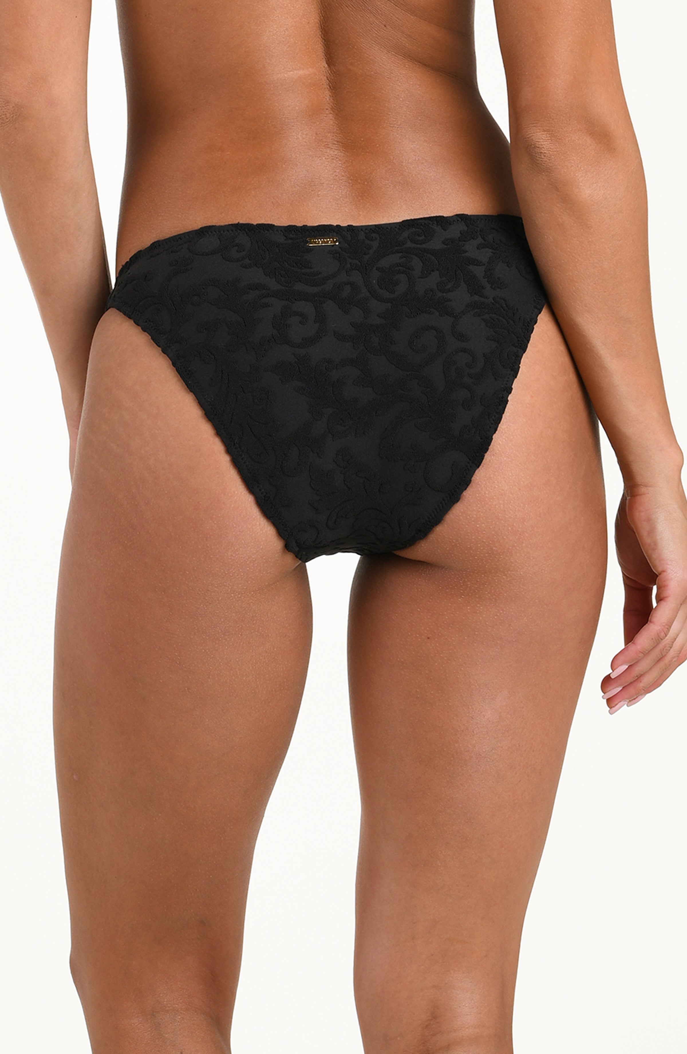 Back image of model wearing a black jacquard bikini bottom featuring a mid-rise fit, scoop front, high leg, gold logo hardware on one side, and contemporary rear coverage.