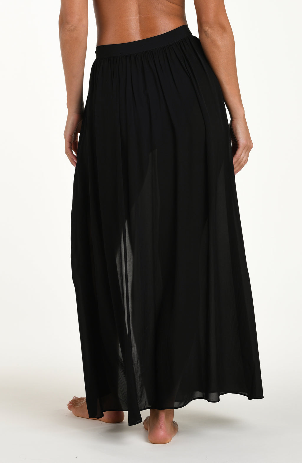 Back image of model wearing a solid black cover up skirt featuring a maxi length and side tie closure. 