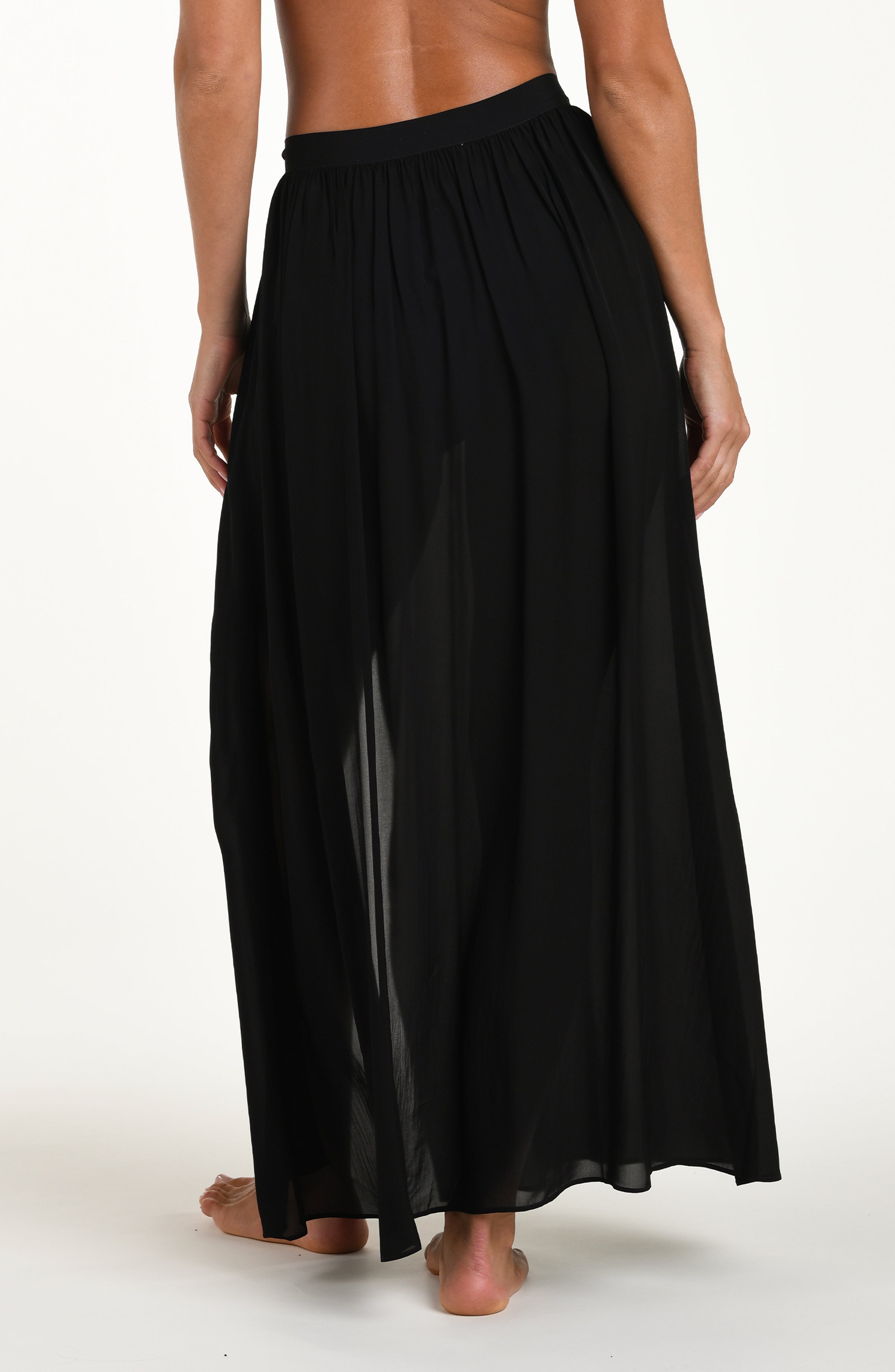 Back image of model wearing a solid black cover up skirt featuring a maxi length and side tie closure. 