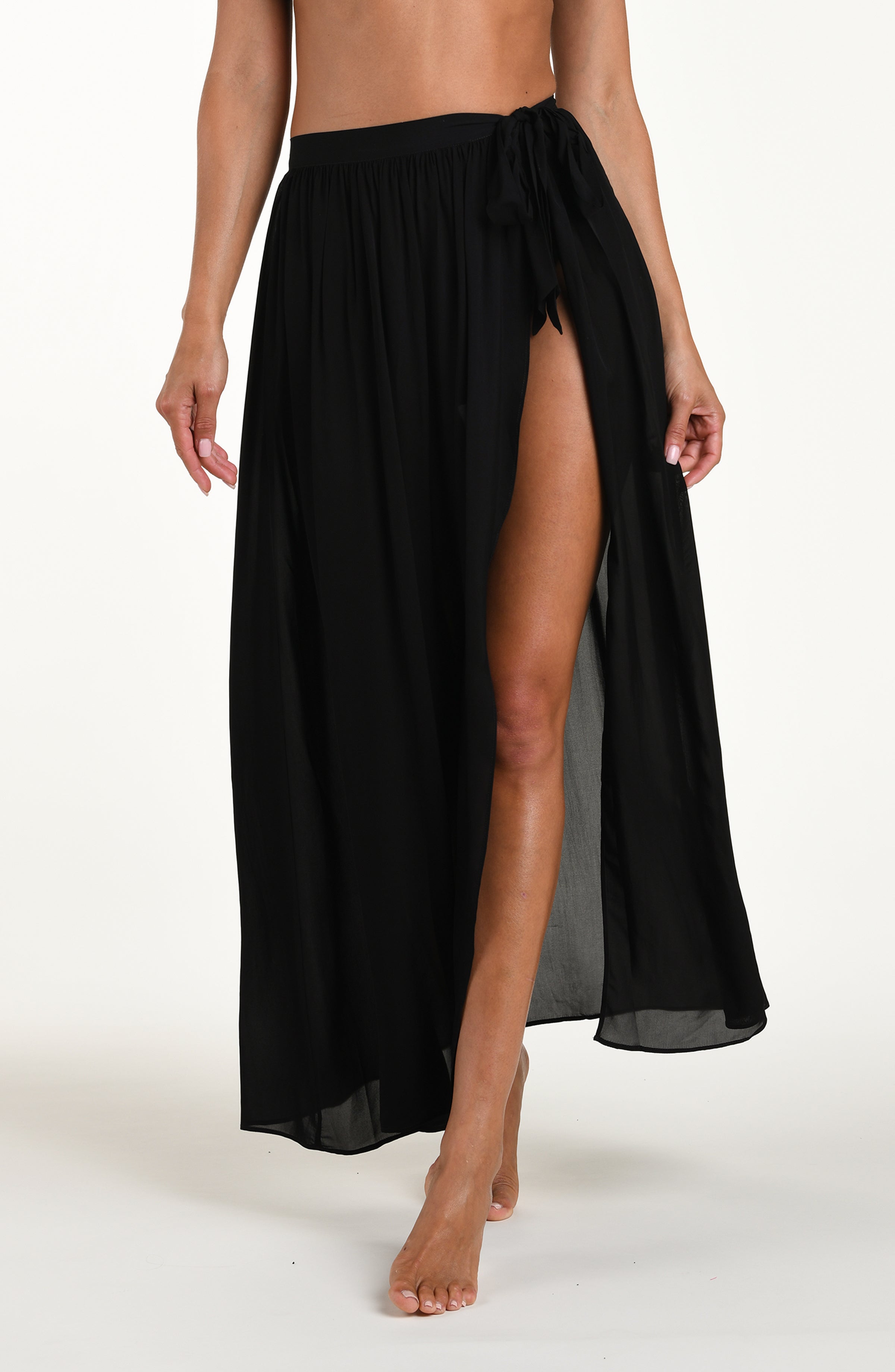 Front image of model wearing a solid black cover up skirt featuring a maxi length and side tie closure. 