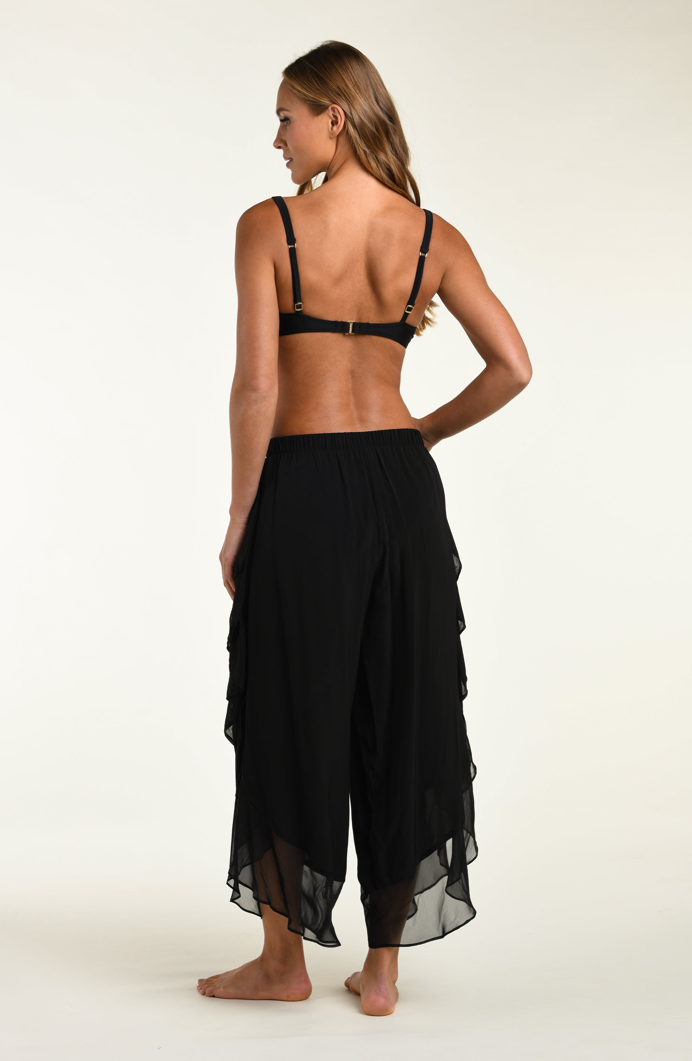 Woman wearing a black strappy top and flowing black pants on a white background