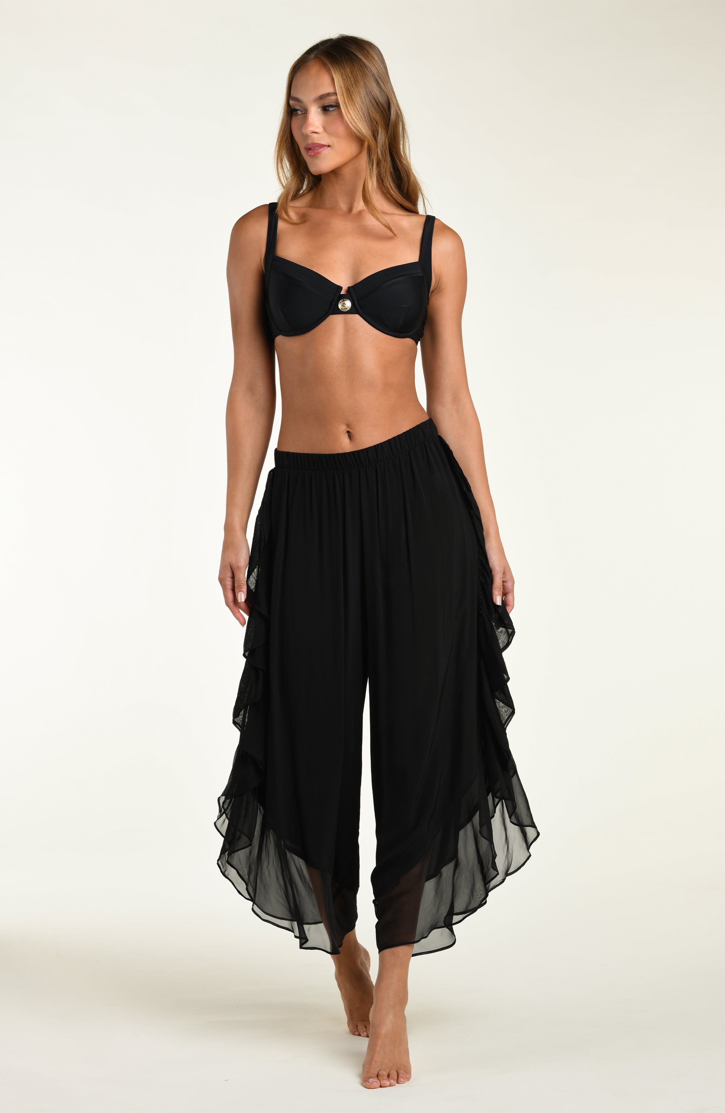 Woman wearing a black bikini top and sheer black pants on a white background
