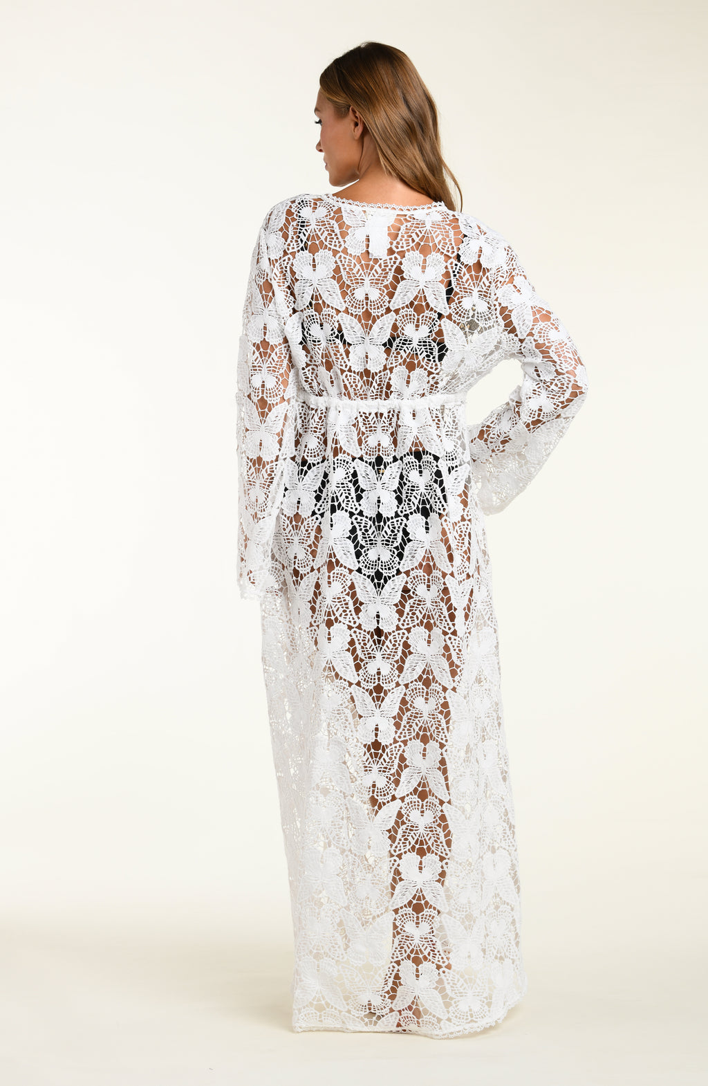 Woman wearing a white lace cover-up over a black bikini on a white background