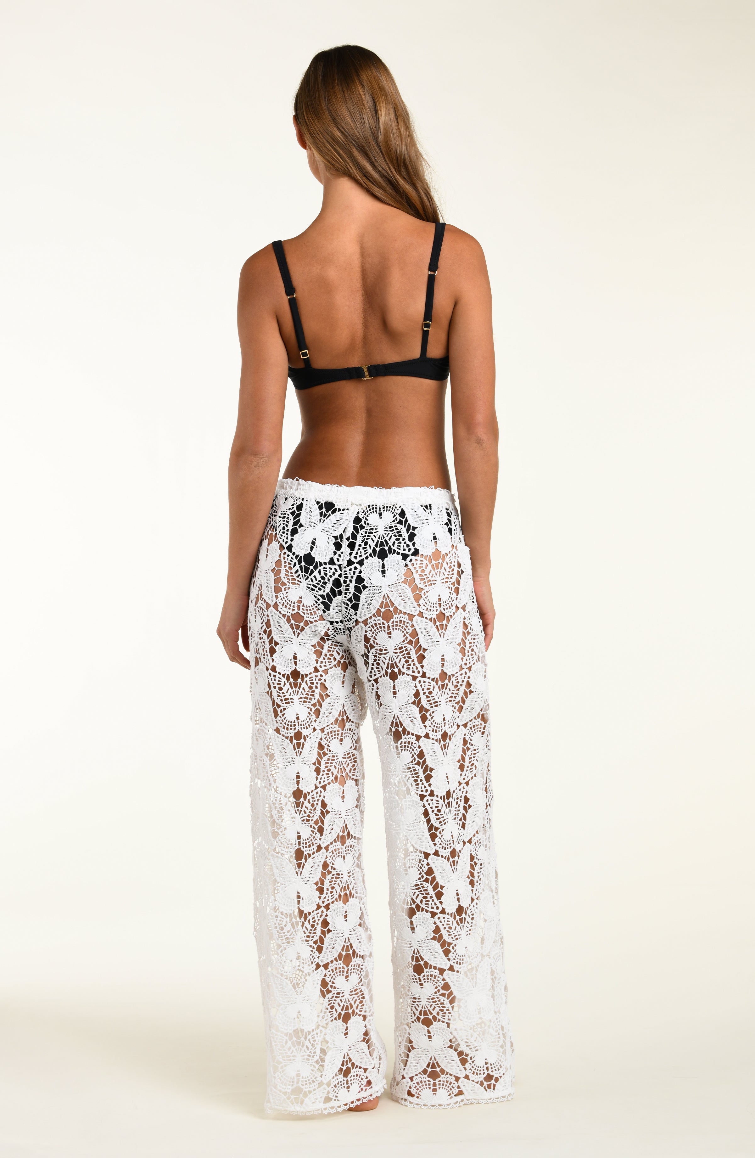 Woman wearing a black bra and white lace pants on a plain background