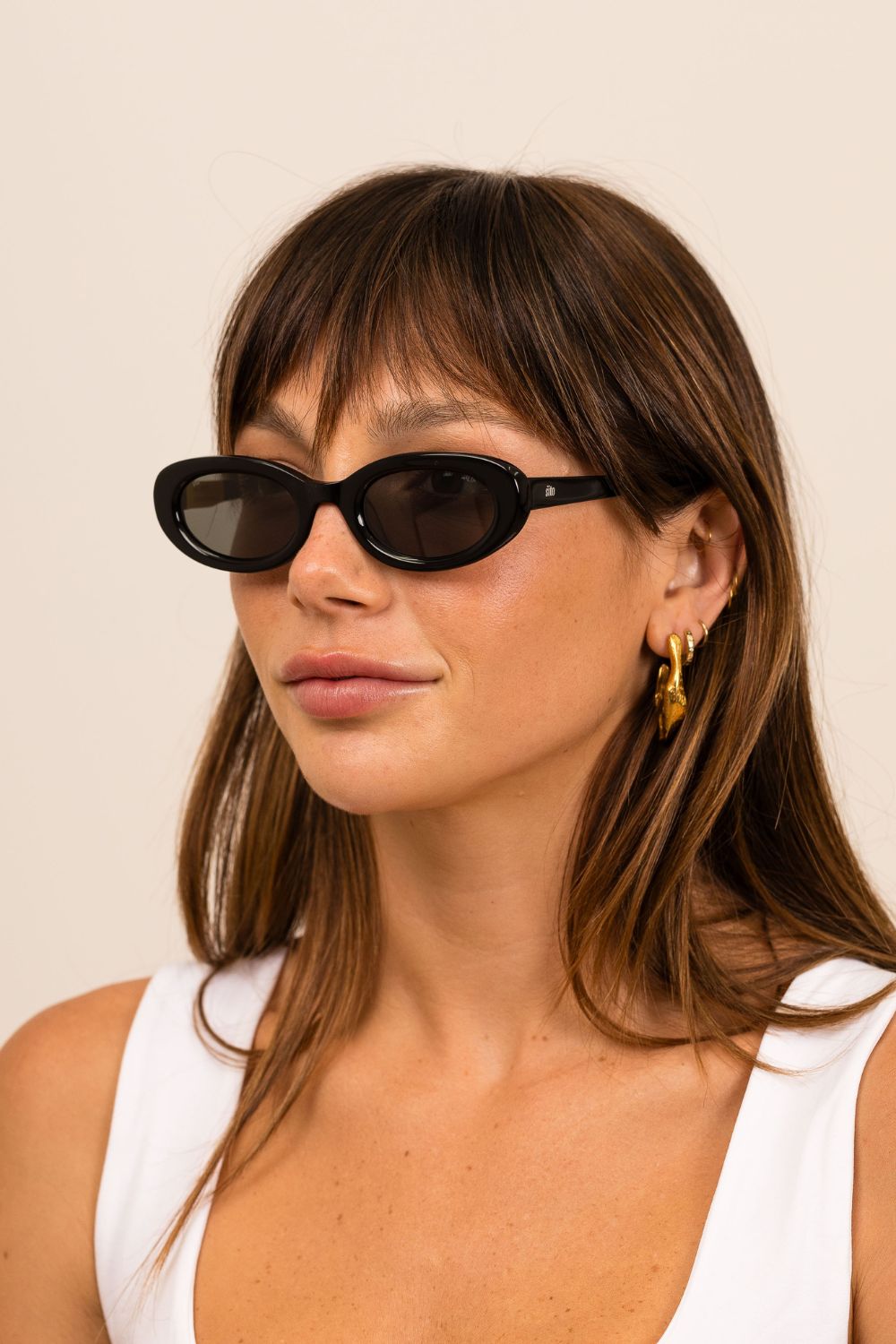 Woman wearing back sunglasses with purple lenses on a white background. 