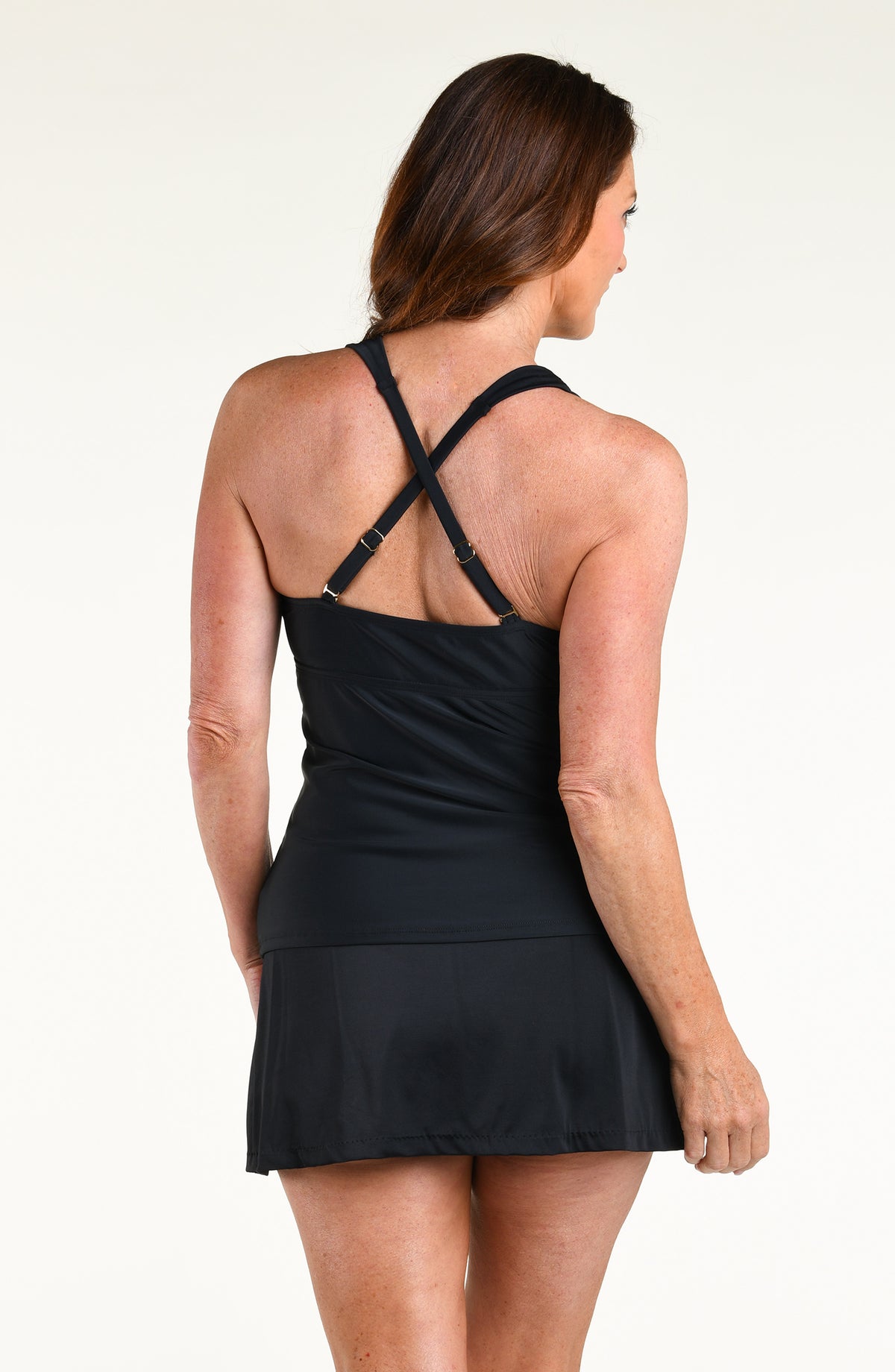 A woman modeling a black halter-neck tankini top and matching swim skirt against a plain white studio background.