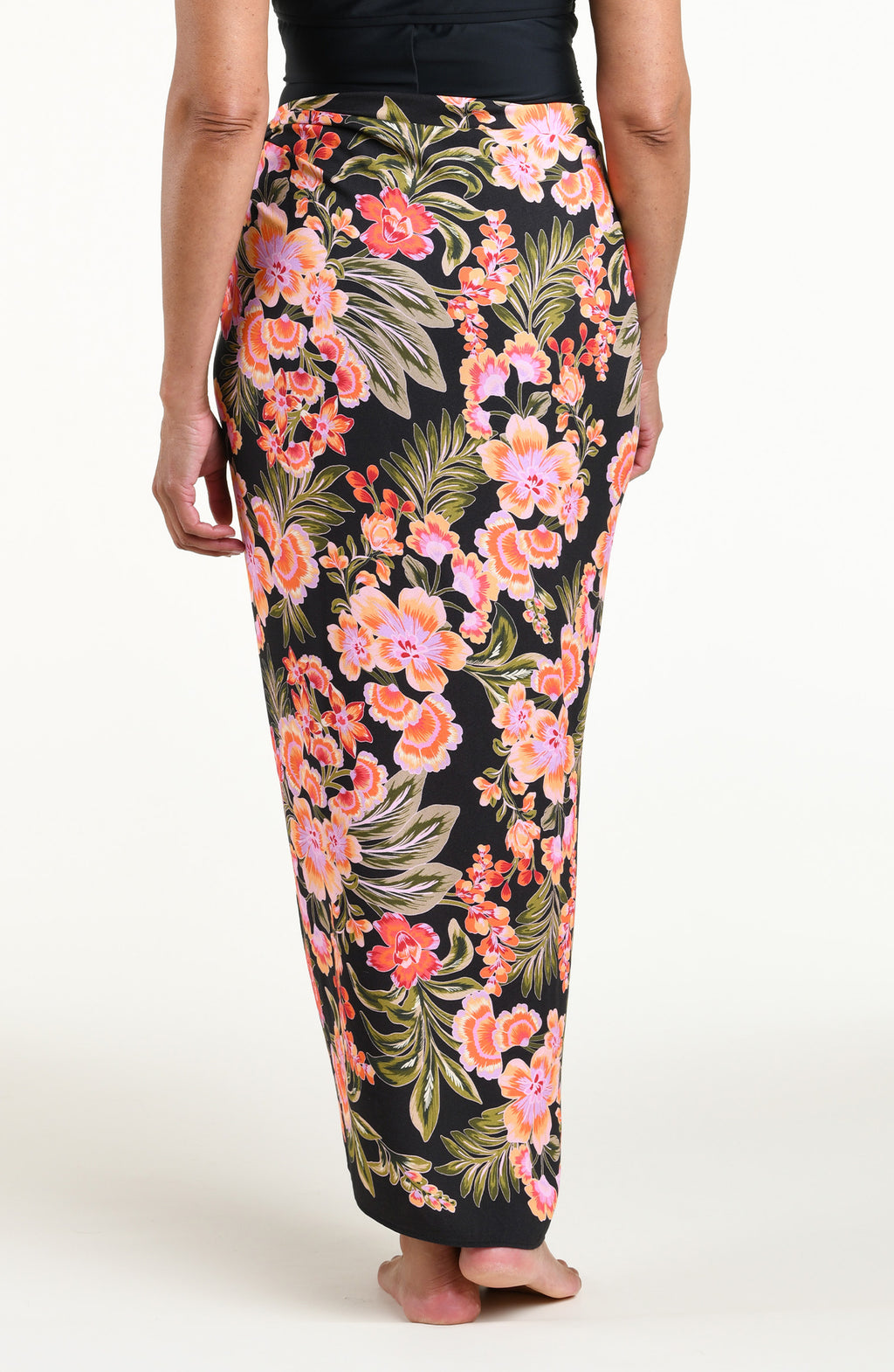 A woman modeling a black wrap sarong with a vibrant pink, orange, and green floral print, featuring a high side slit and a tied waist.