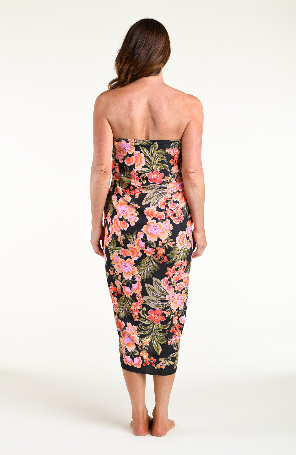 A woman modeling a black wrap sarong with a vibrant pink, orange, and green floral print, featuring a high side slit and a tied waist.