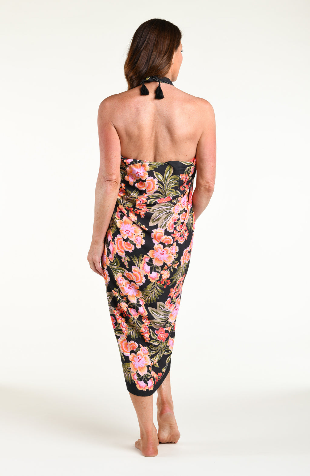 A woman modeling a black wrap sarong with a vibrant pink, orange, and green floral print, featuring a high side slit and a tied waist.