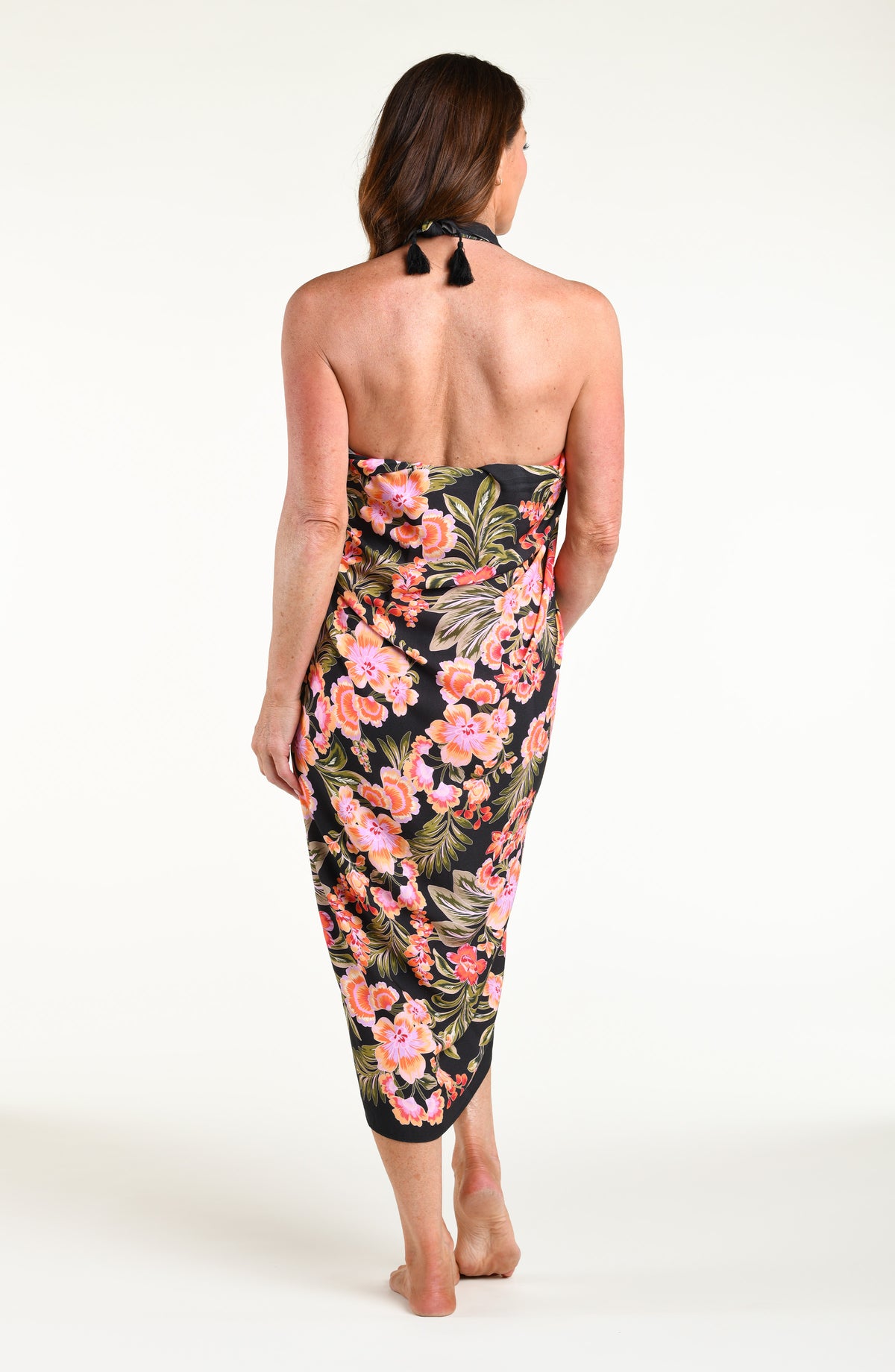 A woman modeling a black wrap sarong with a vibrant pink, orange, and green floral print, featuring a high side slit and a tied waist.