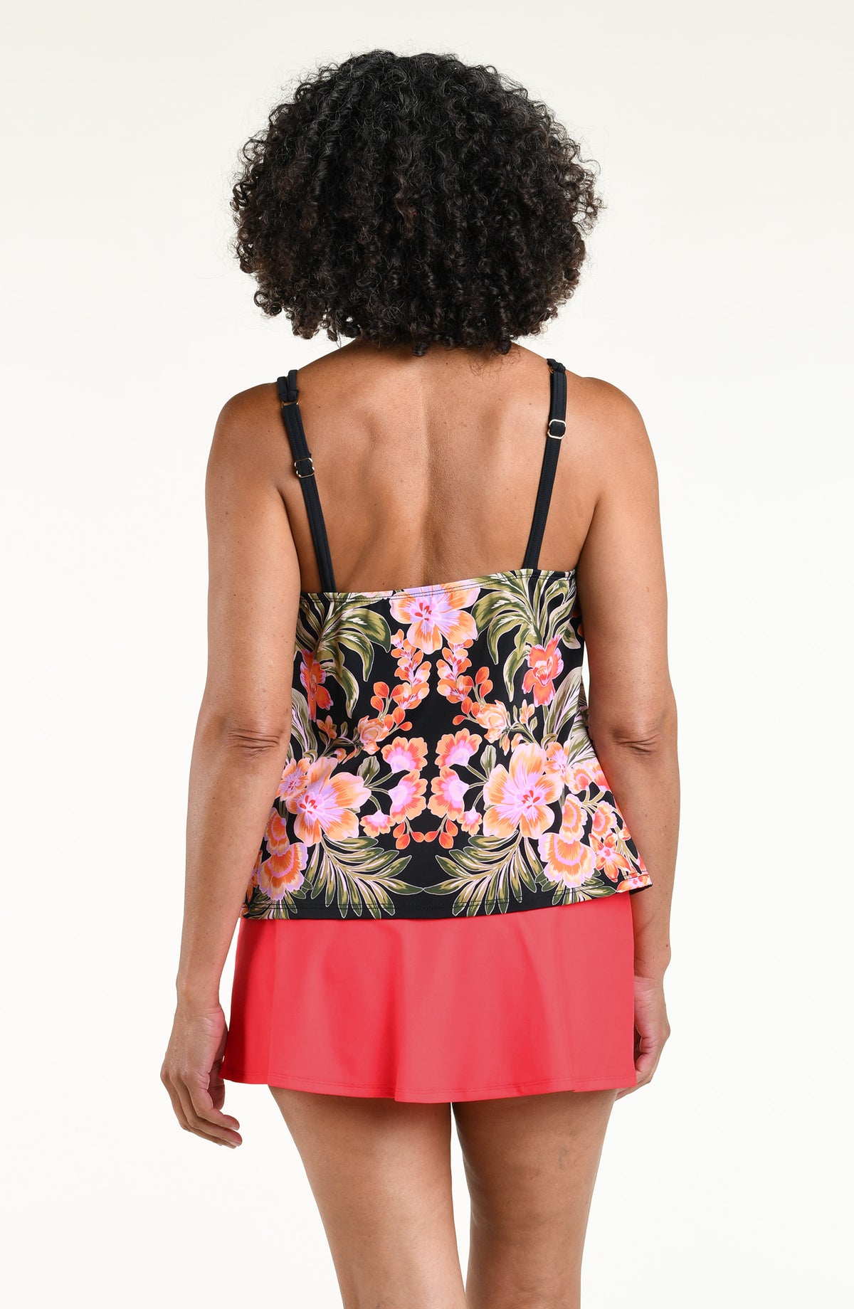 Woman wearing a black multicolored tankini top and solid orange swim skirt against a white background. 
