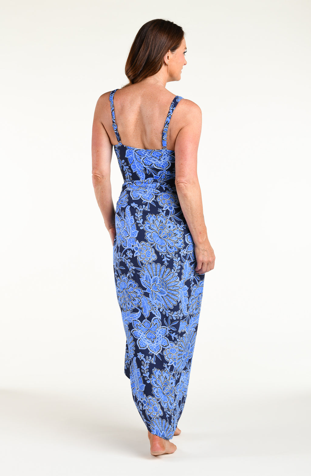 Woman wearing an indigo blue multicolored one piece swimsuit and matching sarong against a white background. 