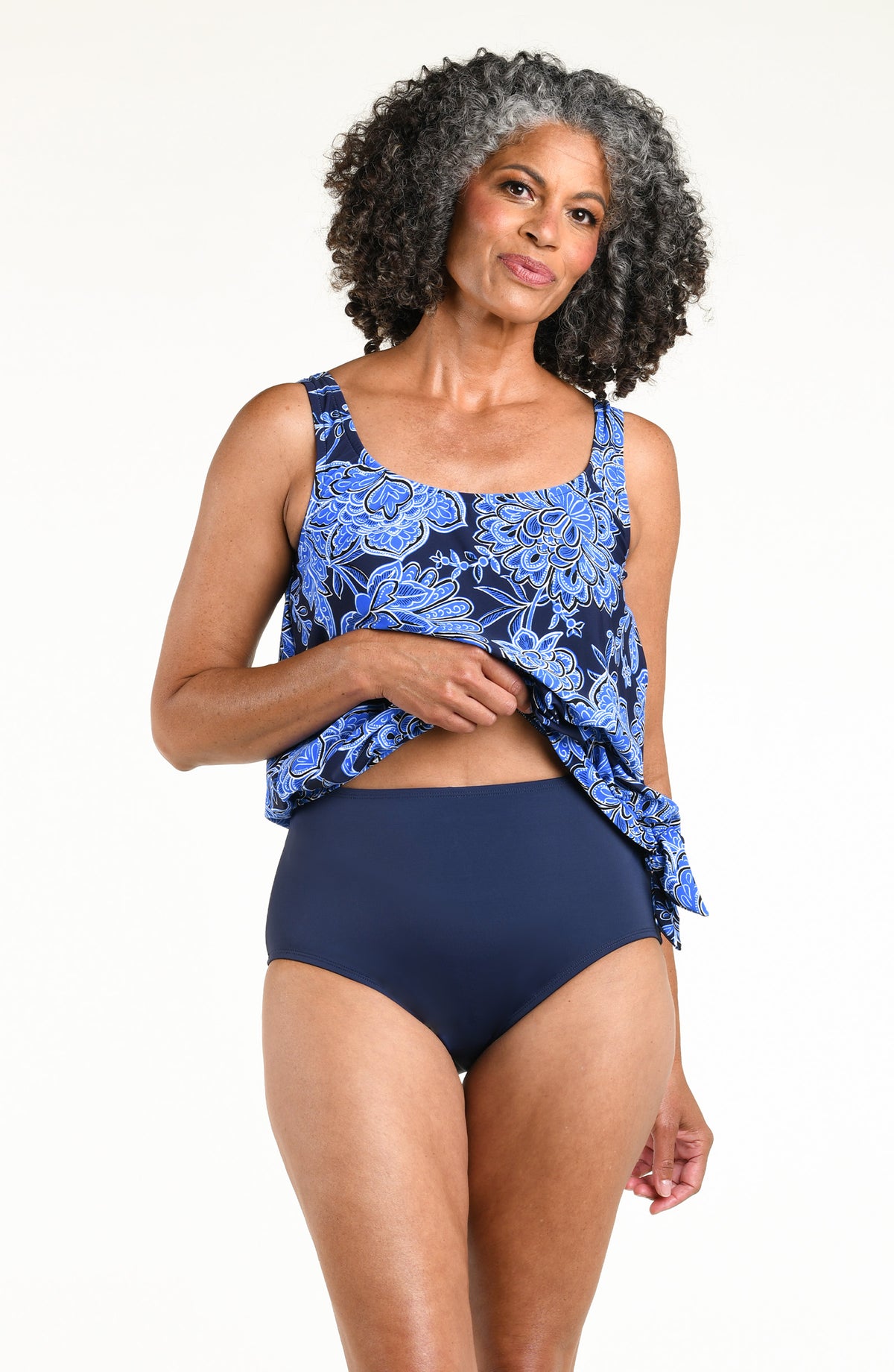 Woman wearing an indigo blue multicolored tankini top and solid indigo blue bikini bottoms against a white background. 
