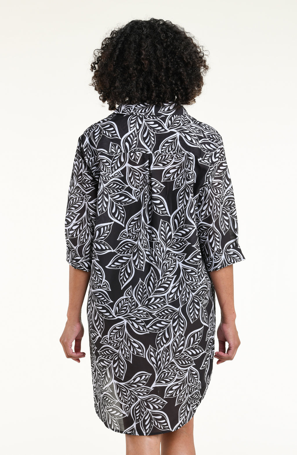 A woman modeling a black and white tropical leaf print tunic with three-quarter sleeves and a high-low hem, shown against a plain white studio background.