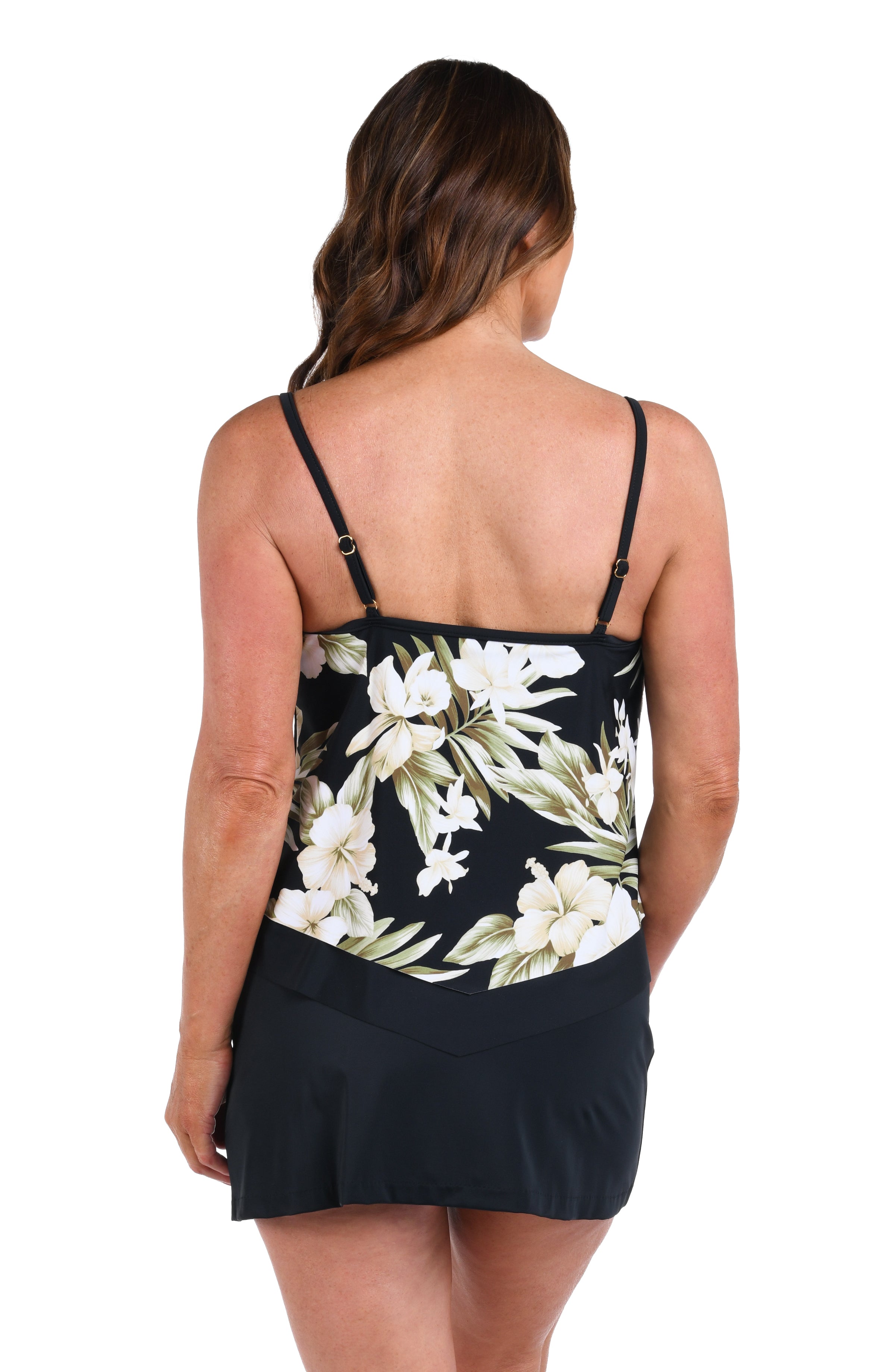 Woman wearing a black floral tankini top with white flowers and green leaves and a black swim skirt against a white background