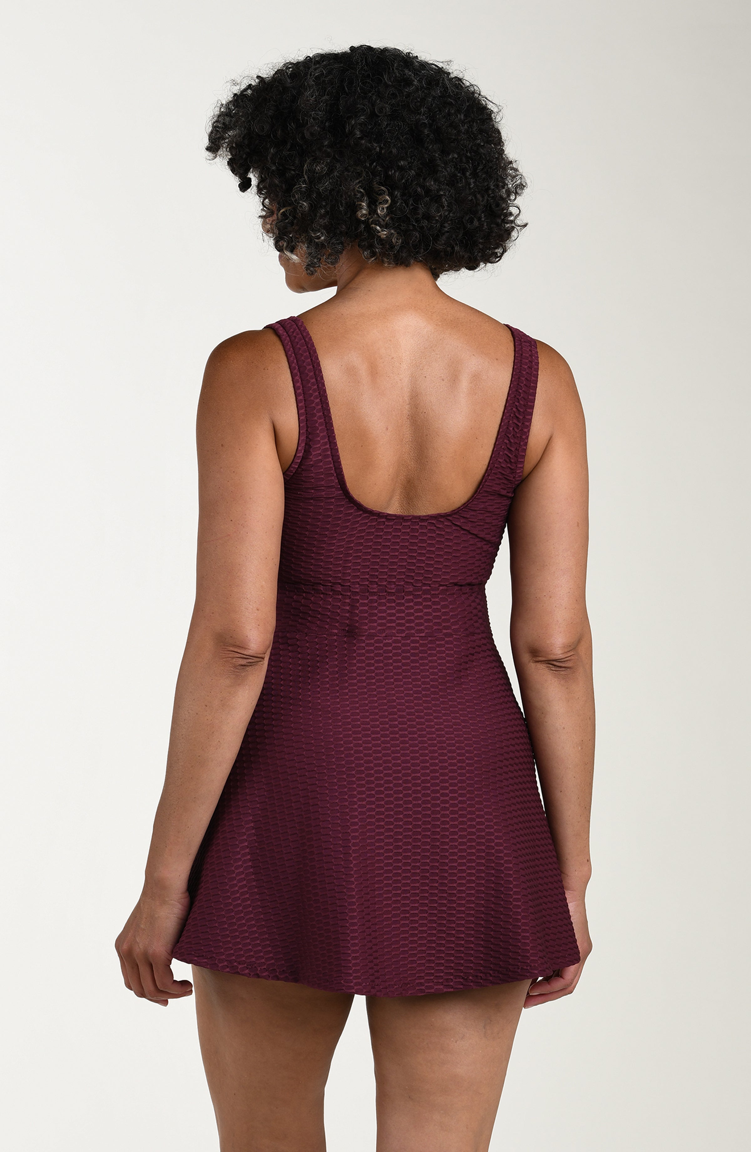 Woman wearing a burgundy dress with a textured pattern on a plain background