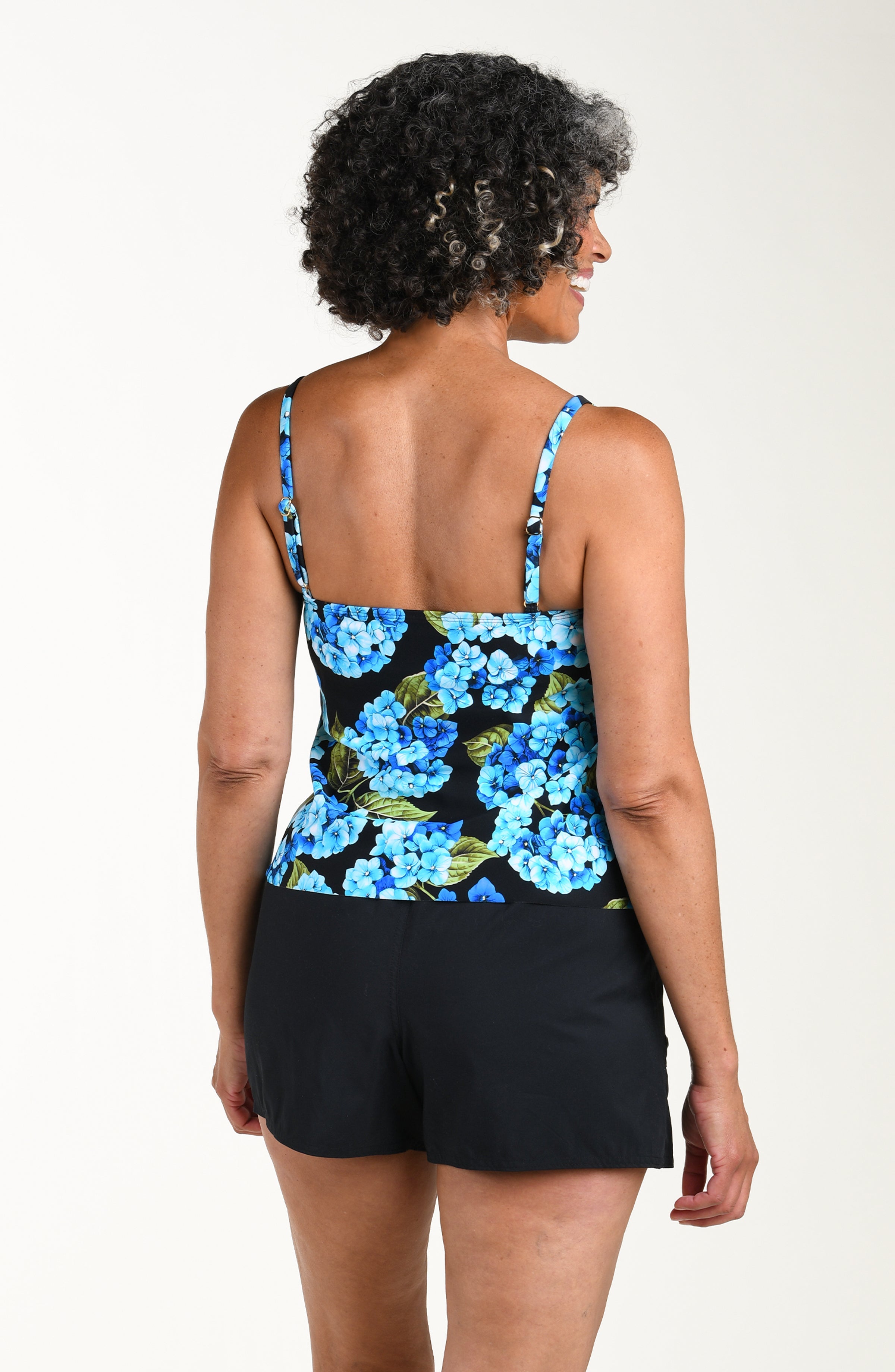 Woman wearing a floral tank top and black shorts on a white background