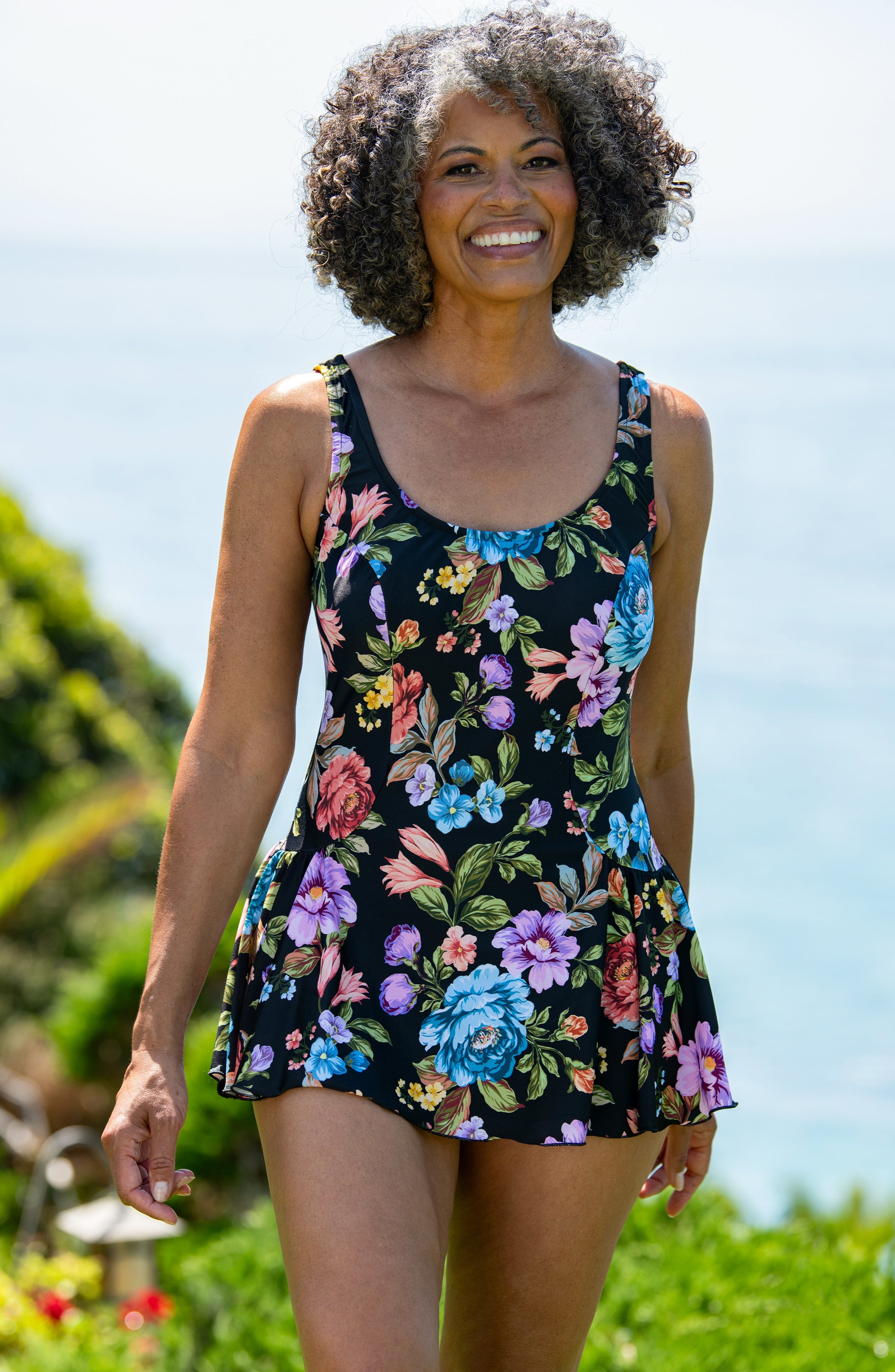 Woman wearing a floral dress standing outdoors with a clear sky and greenery in the background