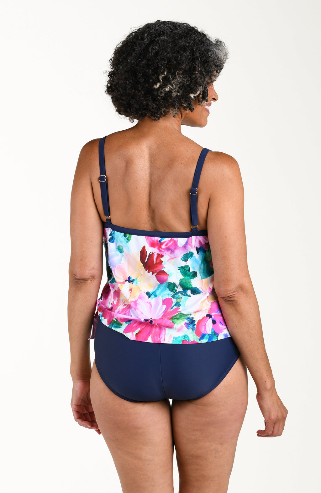 Woman wearing a colorful floral tankini top and navy shorts on a white background